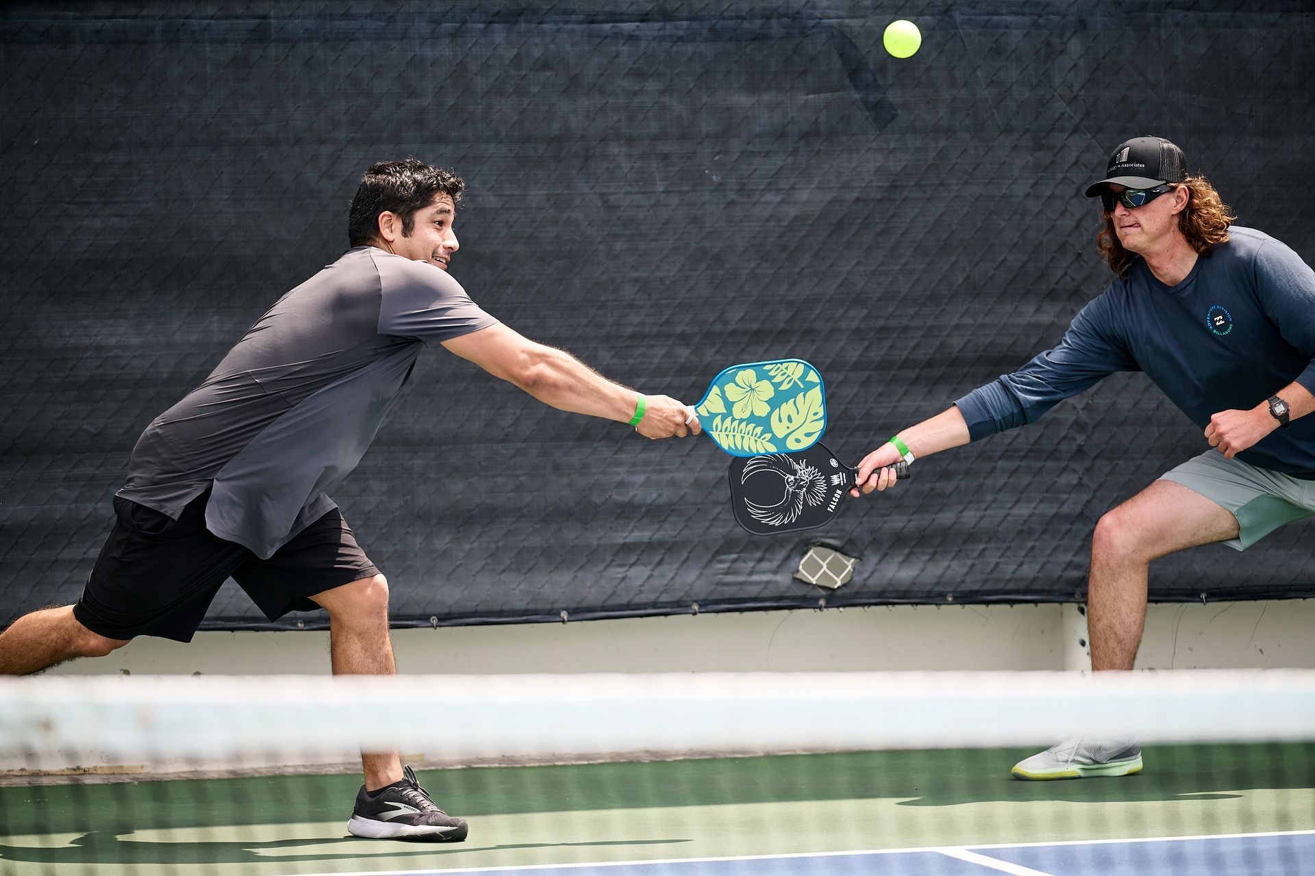 Two pickleball players lunging to return a shot on an indoor court, ball midair near the net