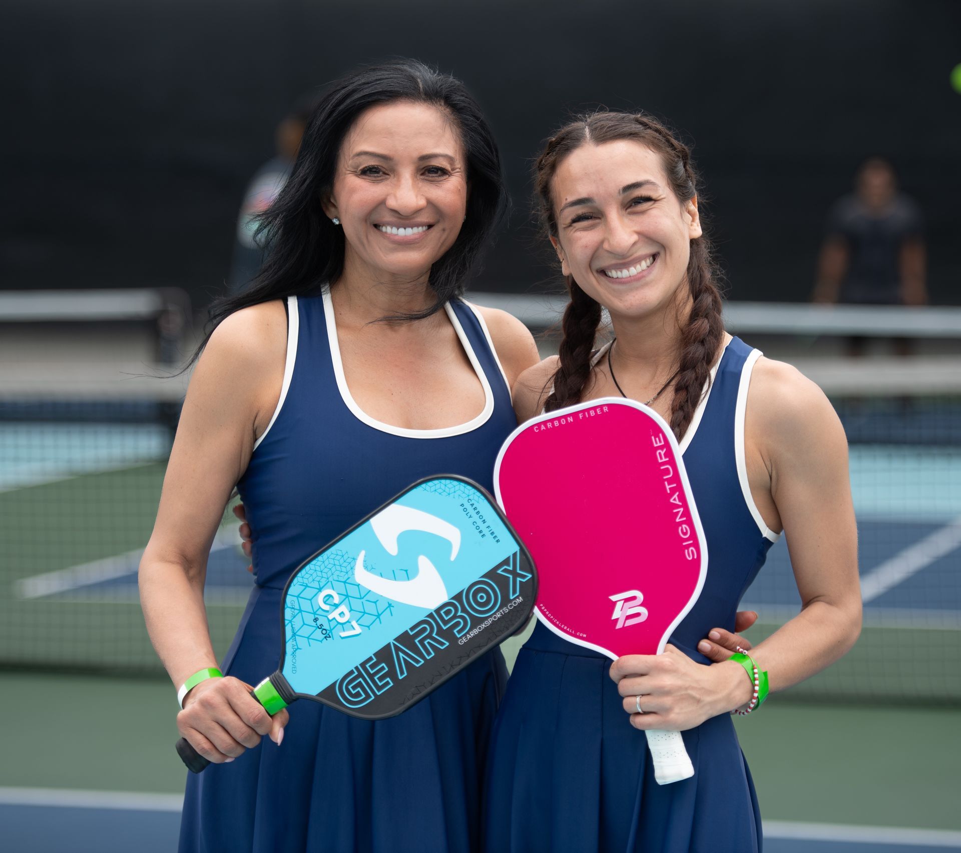 Two padel players smiling on court, holding colorful paddles.