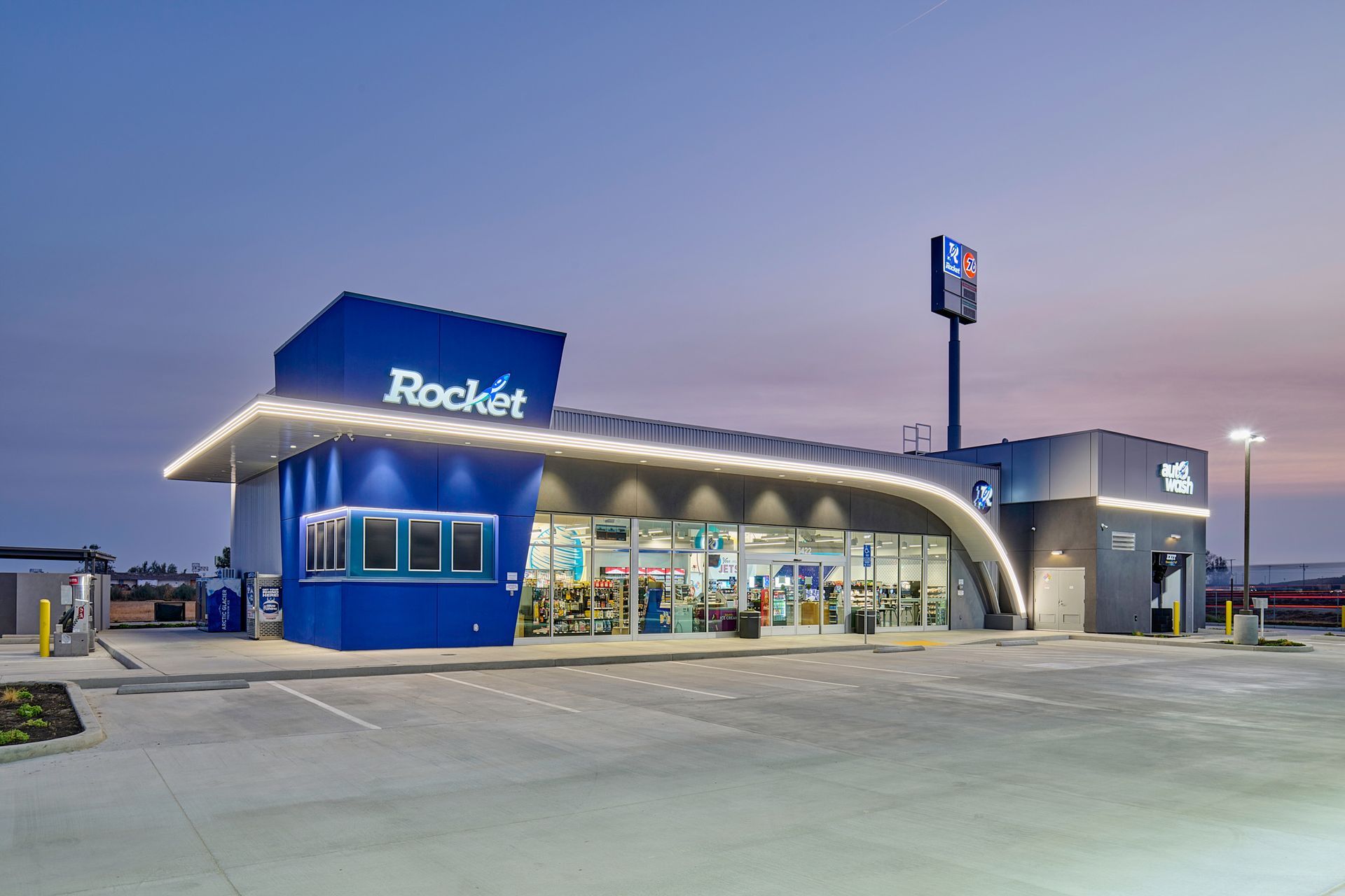 Rocket gas station and convenience store at dusk, with bright blue and gray exterior and lit windows.