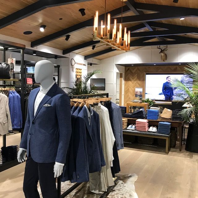 Mannequin in navy blazer inside a modern men’s clothing store with wood accents and hanging lights