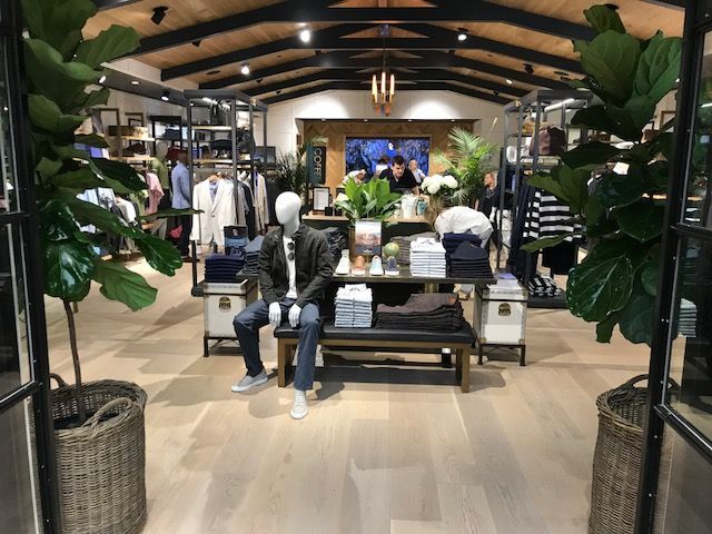 Clothing store interior with mannequins, benches, plants, and a large screen at the back.