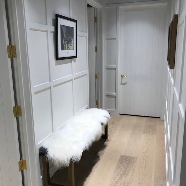 Bright hallway with white paneled walls, a fur-covered bench, and framed art on the wall.
