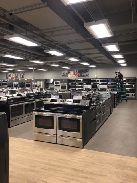Electronics store with rows of appliances and bright overhead lights in a showroom.
