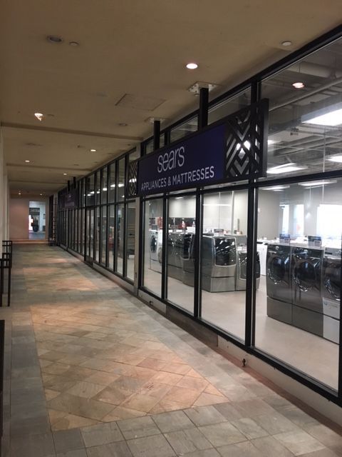 Empty indoor shopping corridor with a storefront labeled “Baker’s” behind glass windows and doors.