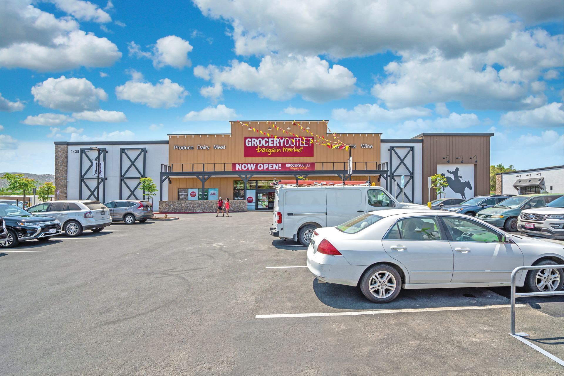 Wide parking lot in front of a store with parked cars under a bright blue sky