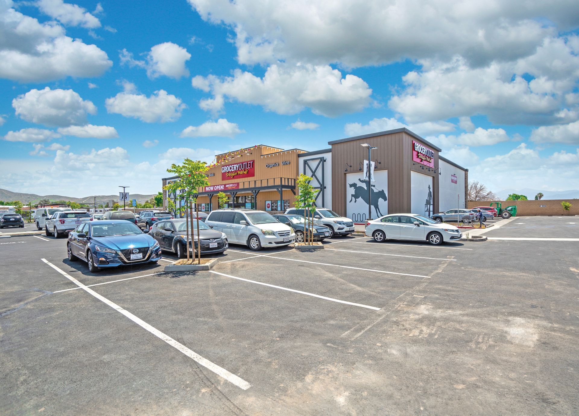 Parking lot outside a retail store with several parked cars under a cloudy blue sky