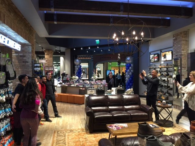 Group of people in a cozy lounge with leather couches, chandeliers, and displayed artwork and products.