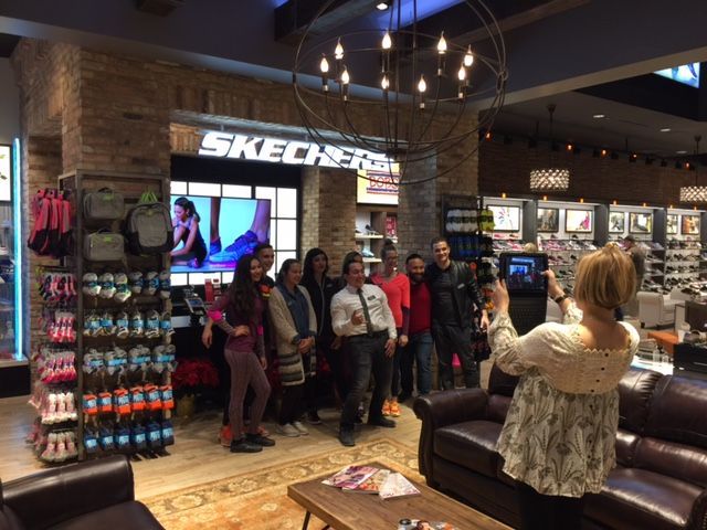 Group posing inside a Skechers store, with sneakers on display and a woman taking their photo.