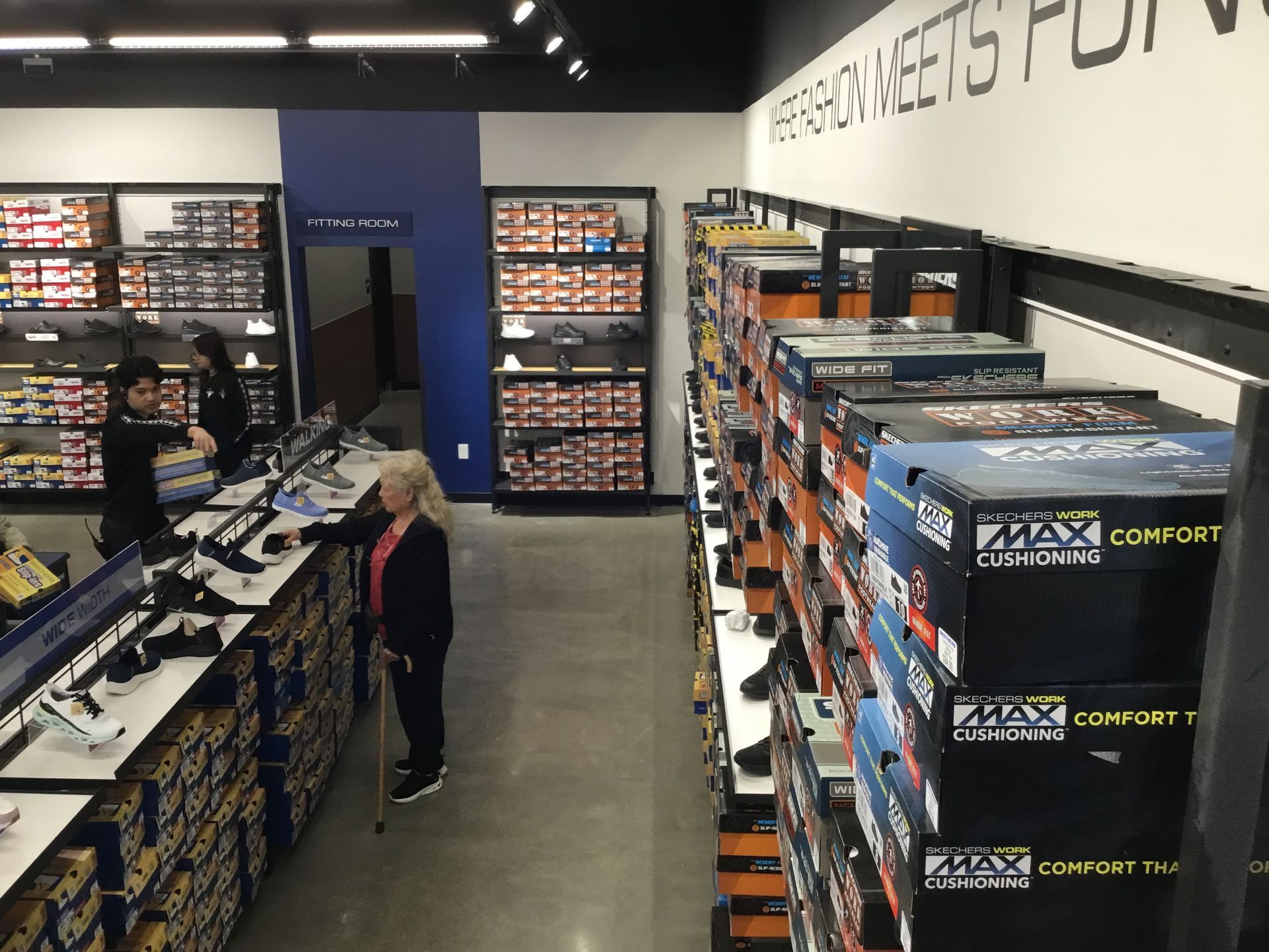 A camera store aisle with shelves of boxed cameras and accessories, and two people browsing inside.