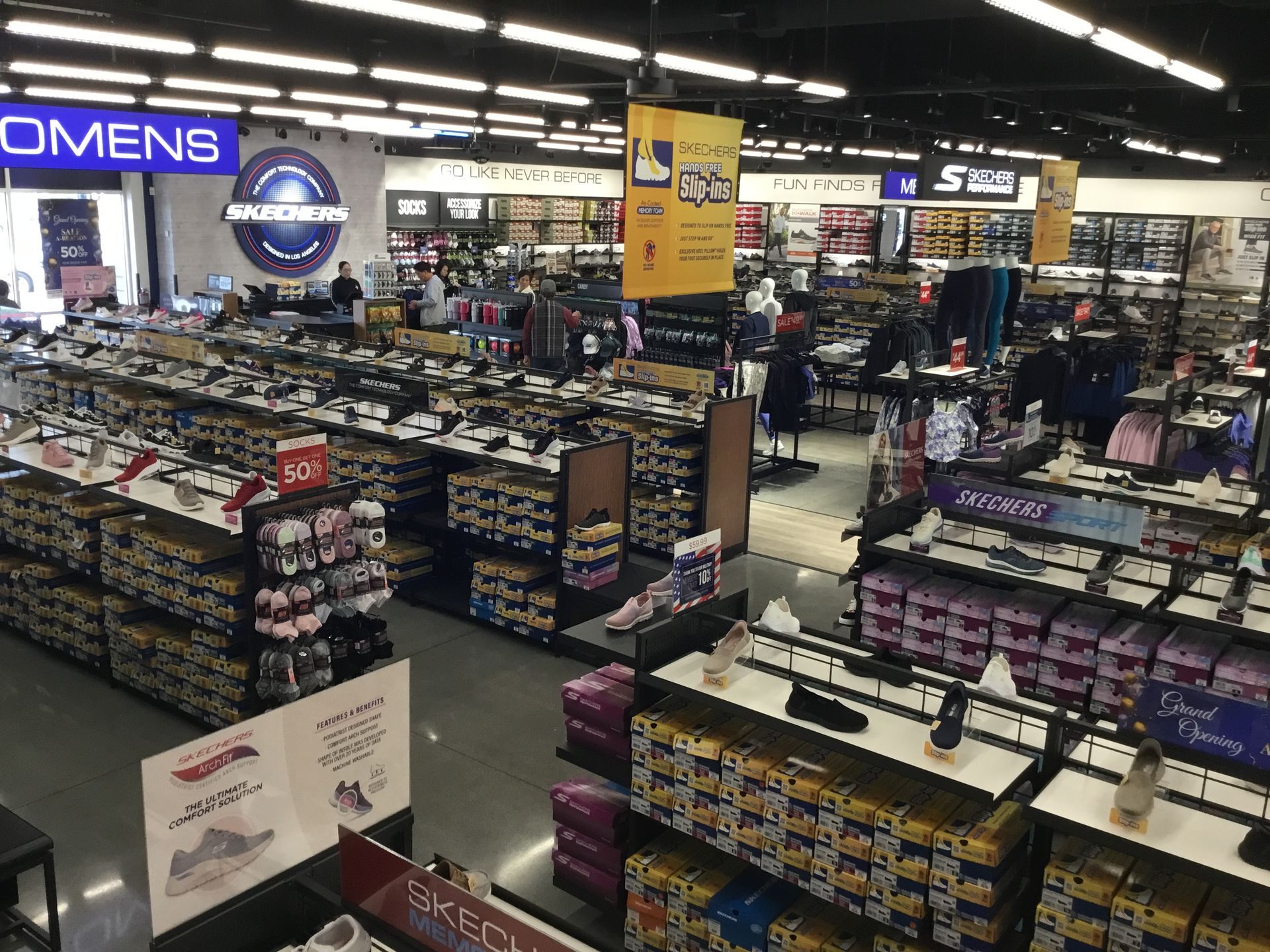 Bright retail store interior with rows of shoes and accessories under overhead lights and OMENS signage