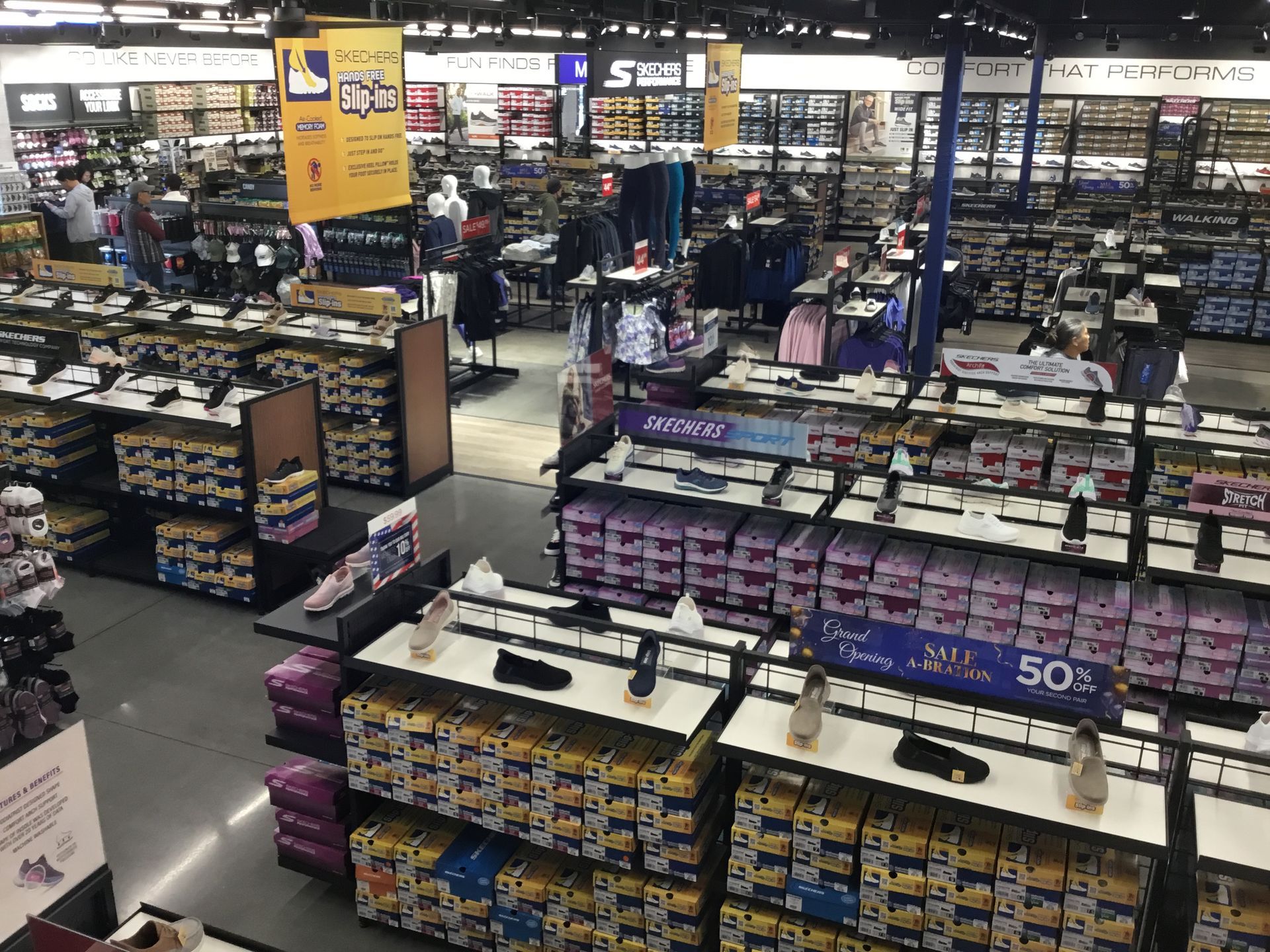 Shoe store aisle with rows of sneakers and sale signs under bright fluorescent lights