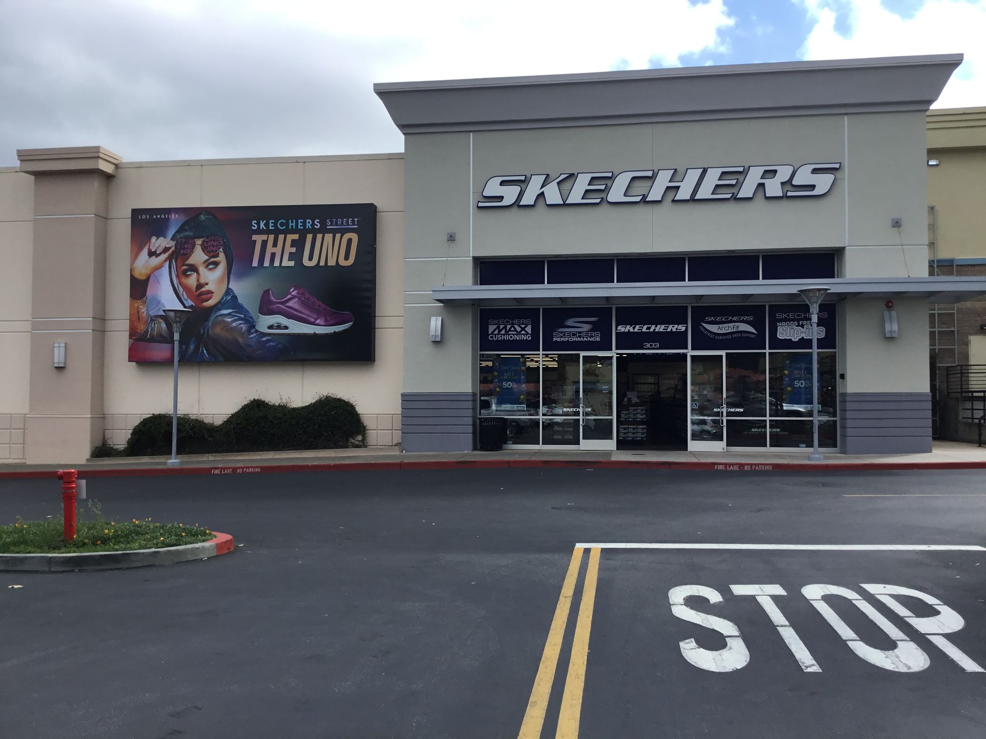 Skechers store exterior with a movie poster, glass entrance, and STOP marking in the parking lot.