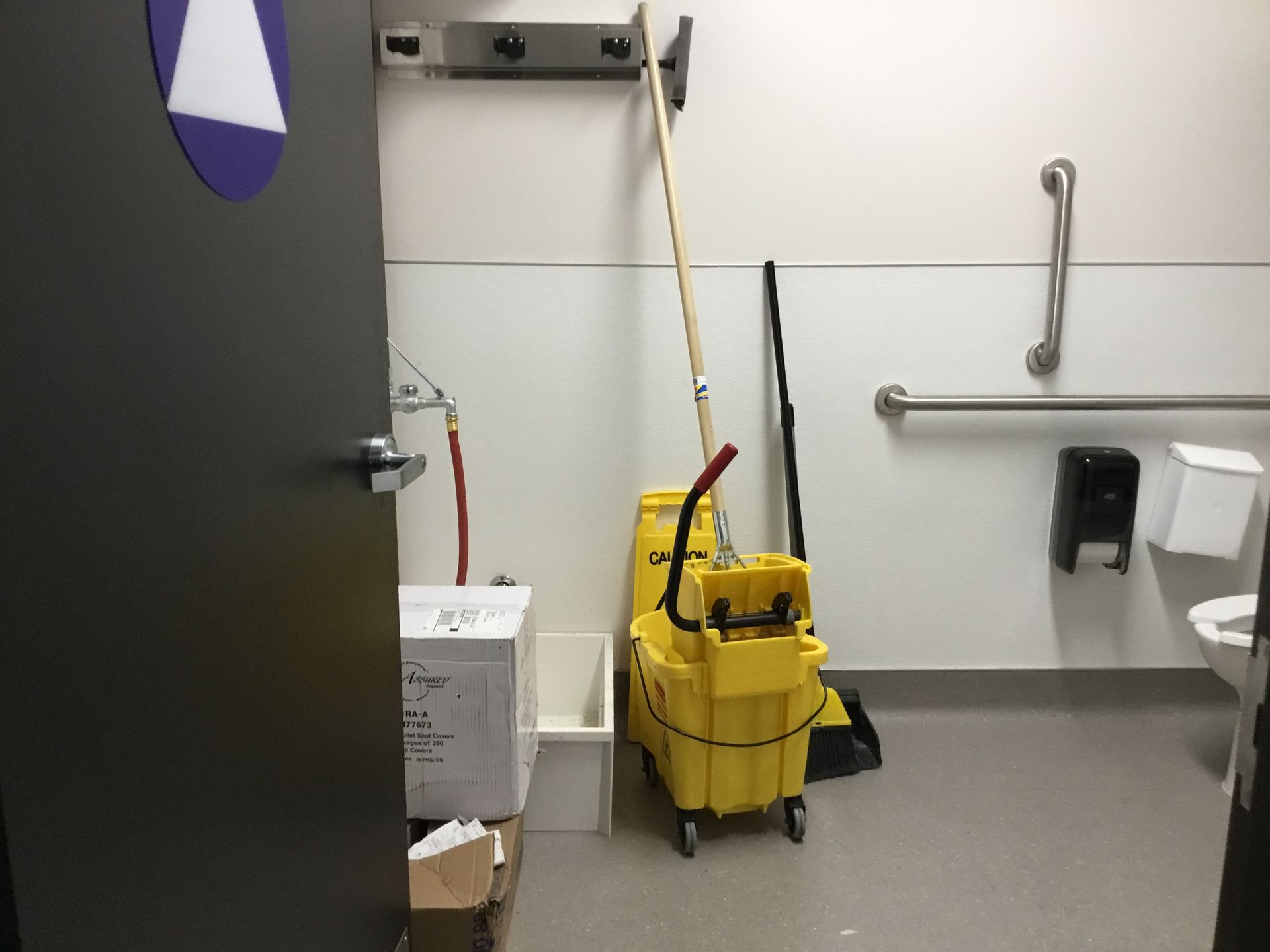 Janitor cart with mop in a restroom beside a sink, toilet, and open door