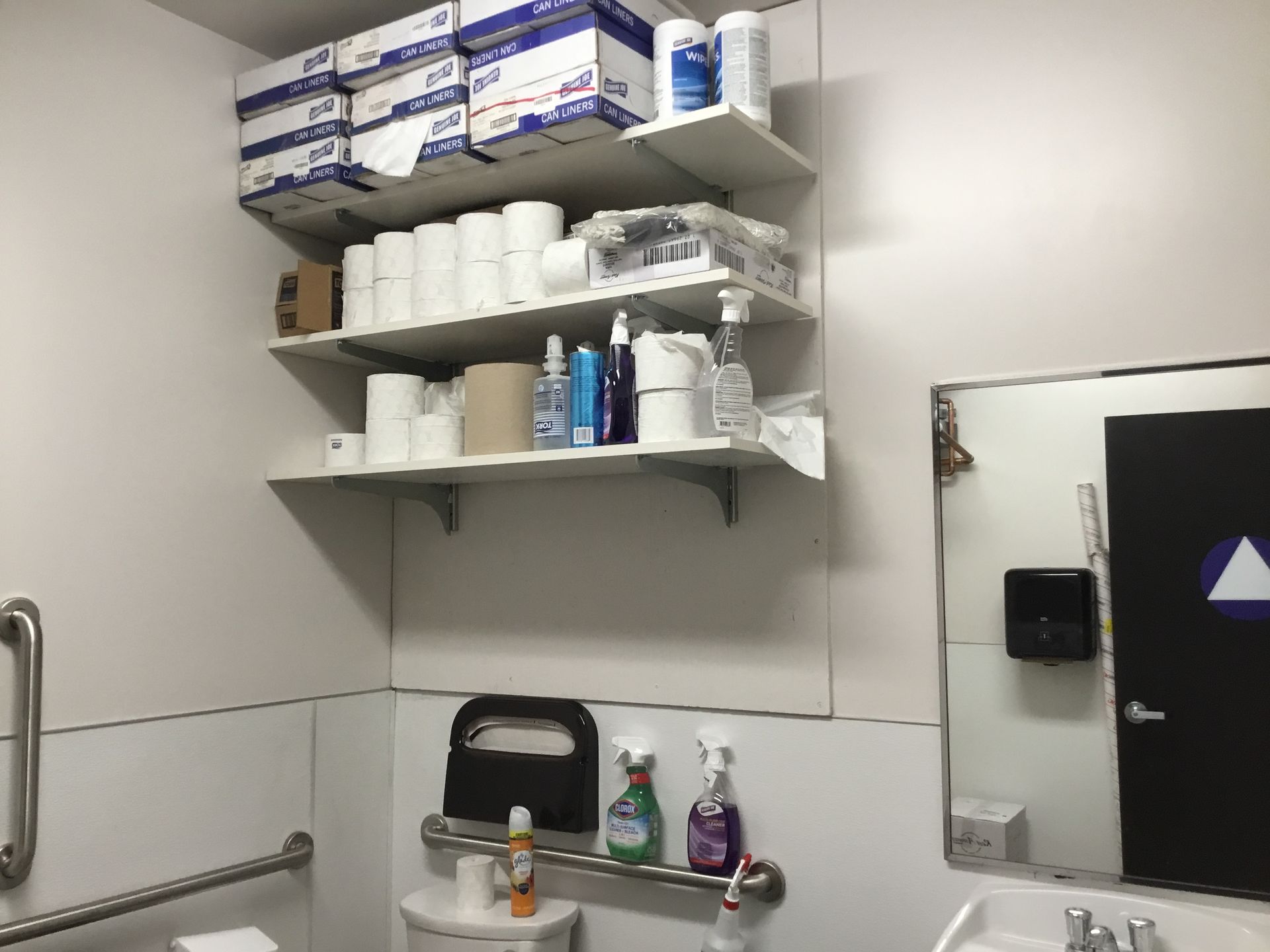 Small bathroom corner with shelves of toiletries, toilet paper, a sink, and a mirror.