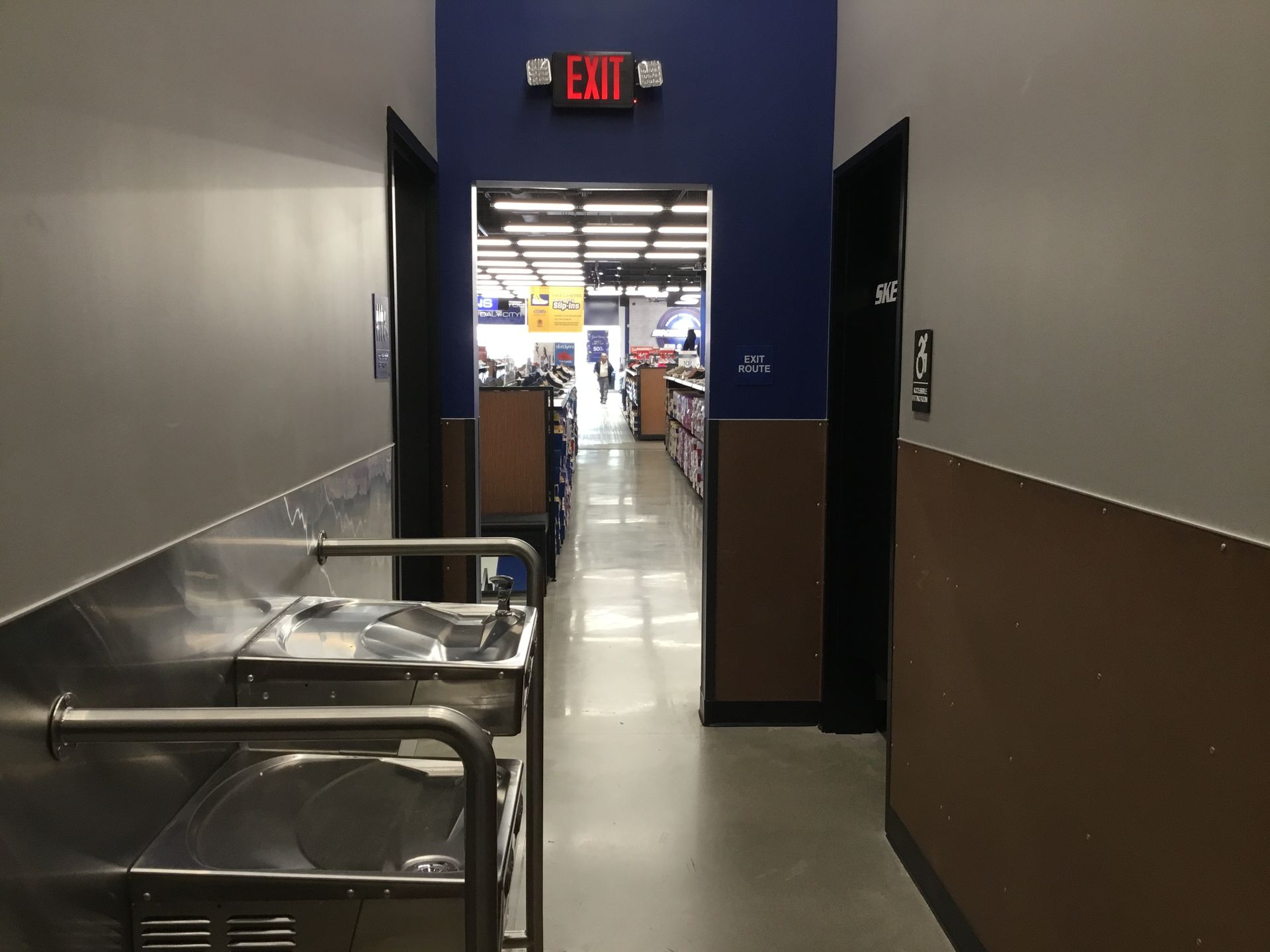 Store hallway leading to a bright exit, with metal carts along the left wall.