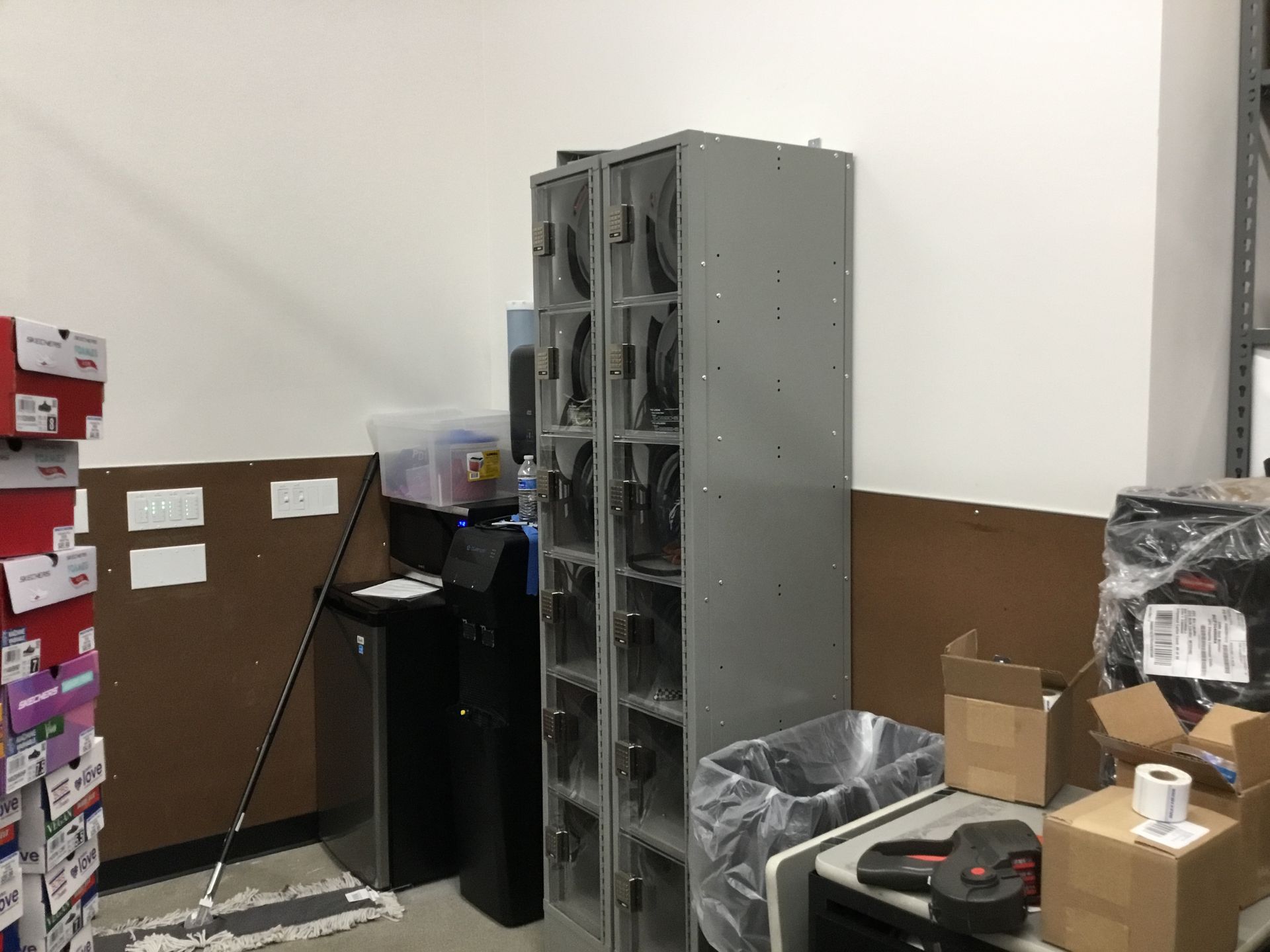 Industrial storage room with stacked metal shelving, boxes, and equipment along a white-and-brown wall