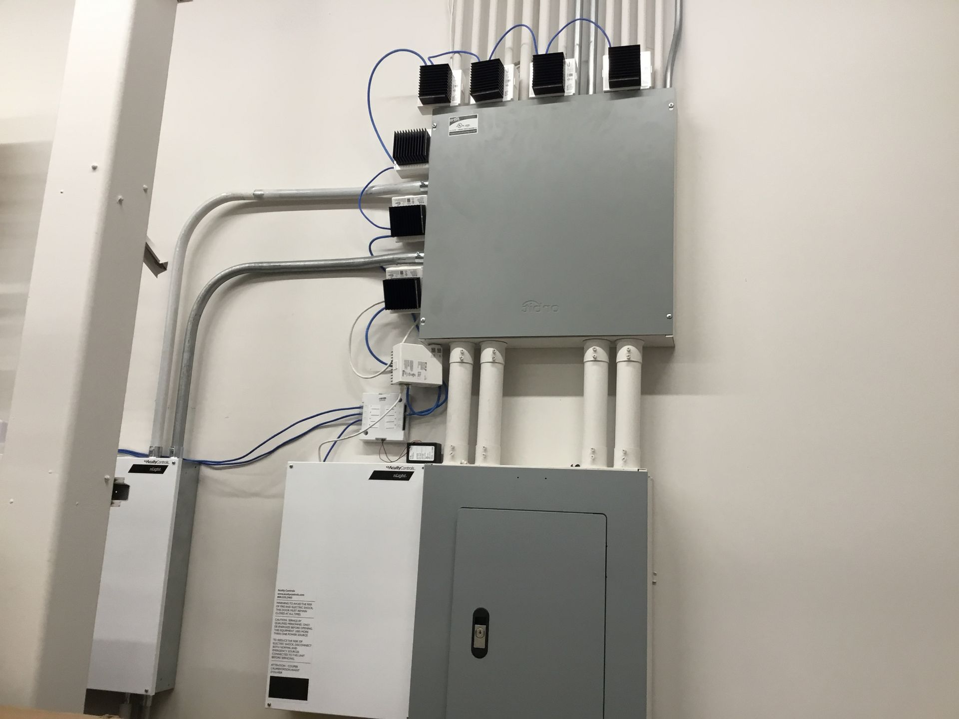 Electrical control boxes and conduit mounted on a wall in a utility room.