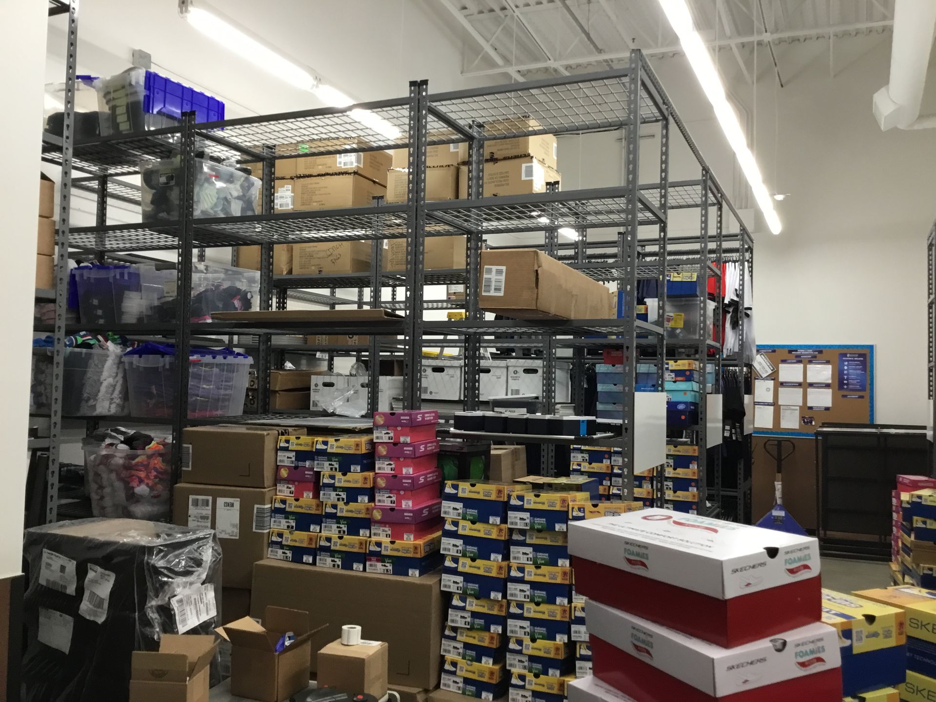 Warehouse storage area with metal shelving, stacked boxes, and supplies under bright ceiling lights