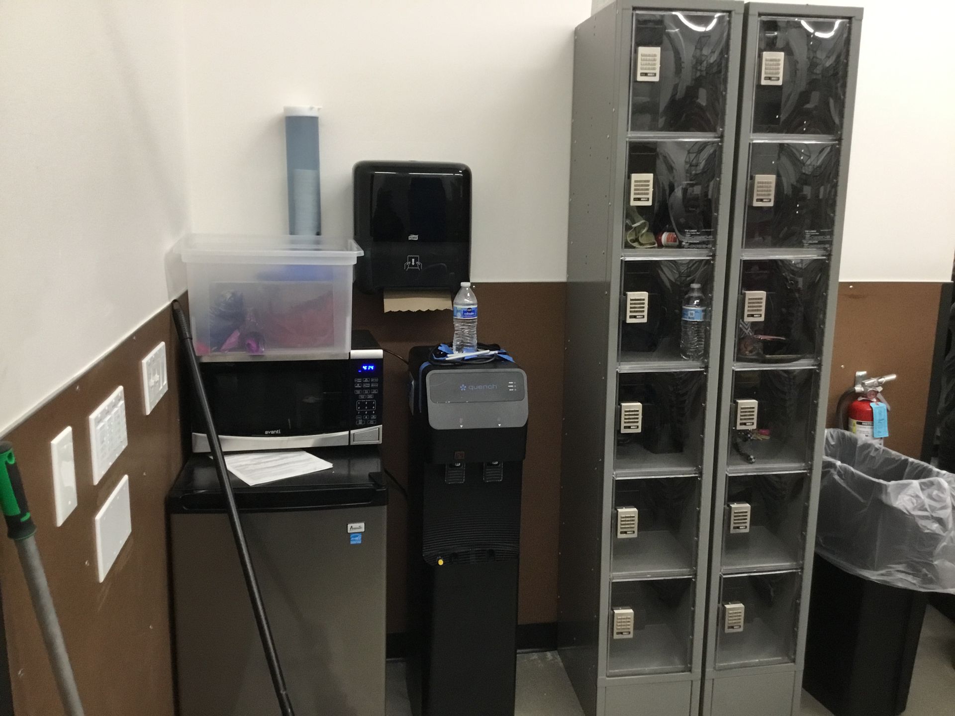 Small office corner with a desk, black water cooler, and stacked clear drawer organizers against a white wall