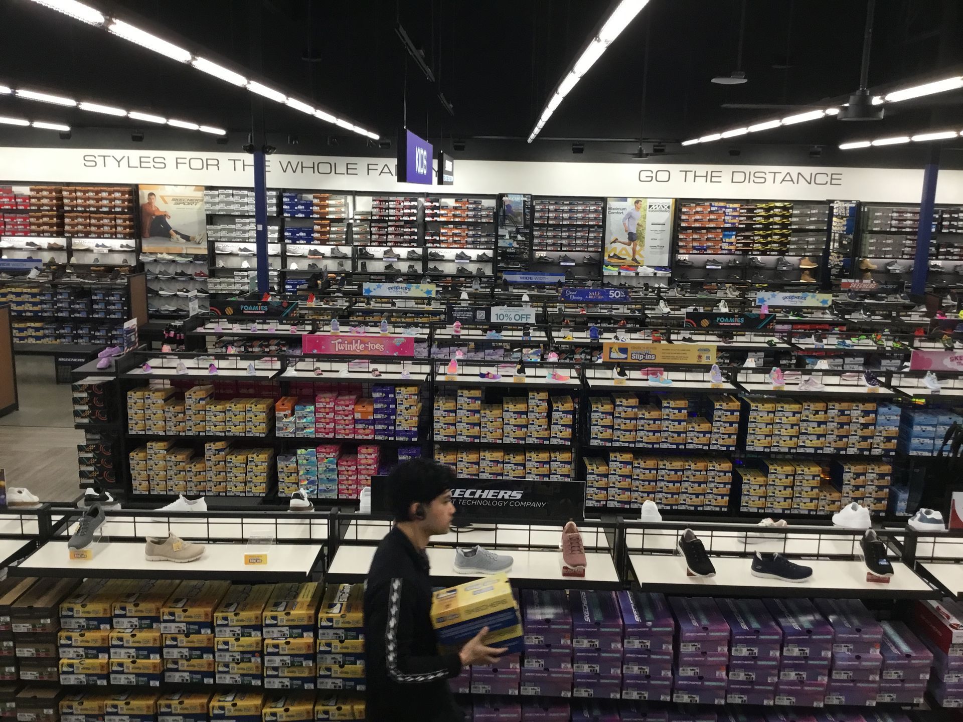 Store aisle with shelves of electronics and a person walking by in the foreground.