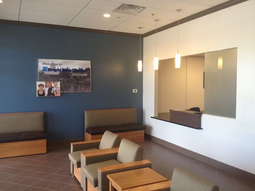 Empty waiting room with brown benches, beige chairs, blue wall, and a reception window.