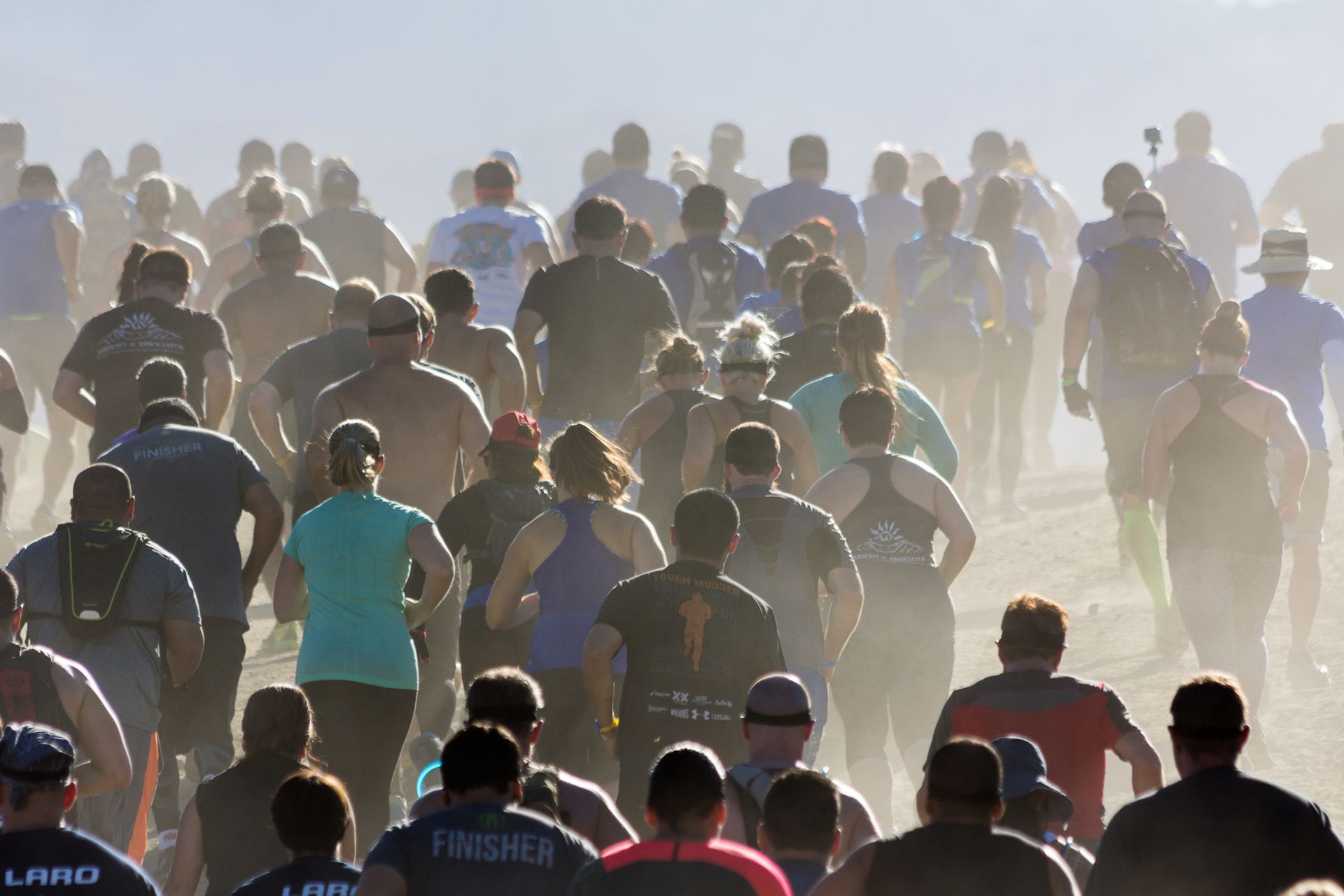Crowd of runners moving through a dusty outdoor race in bright sunlight