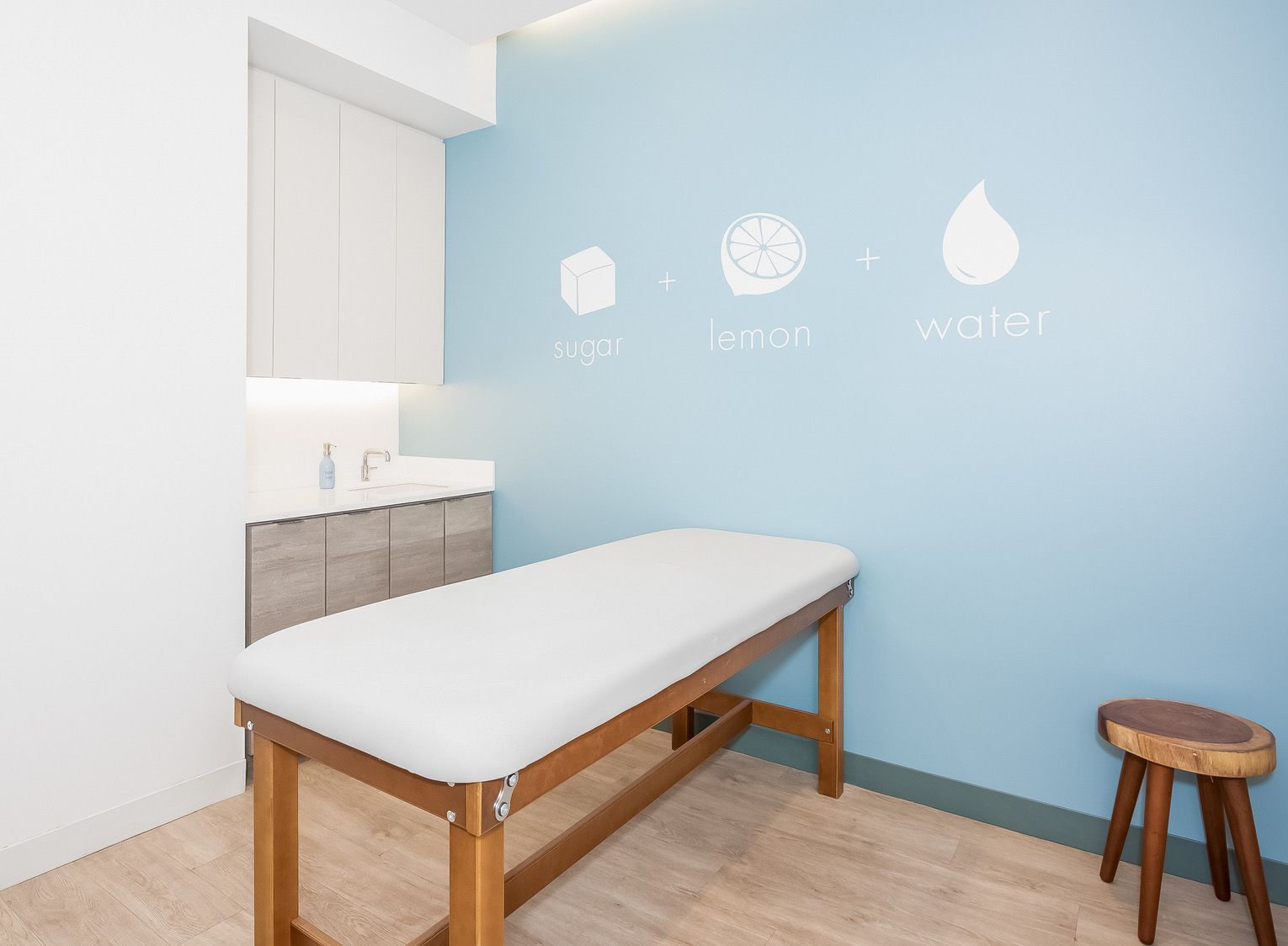 Bright treatment room with blue wall, massage table, sink cabinet, and small stool