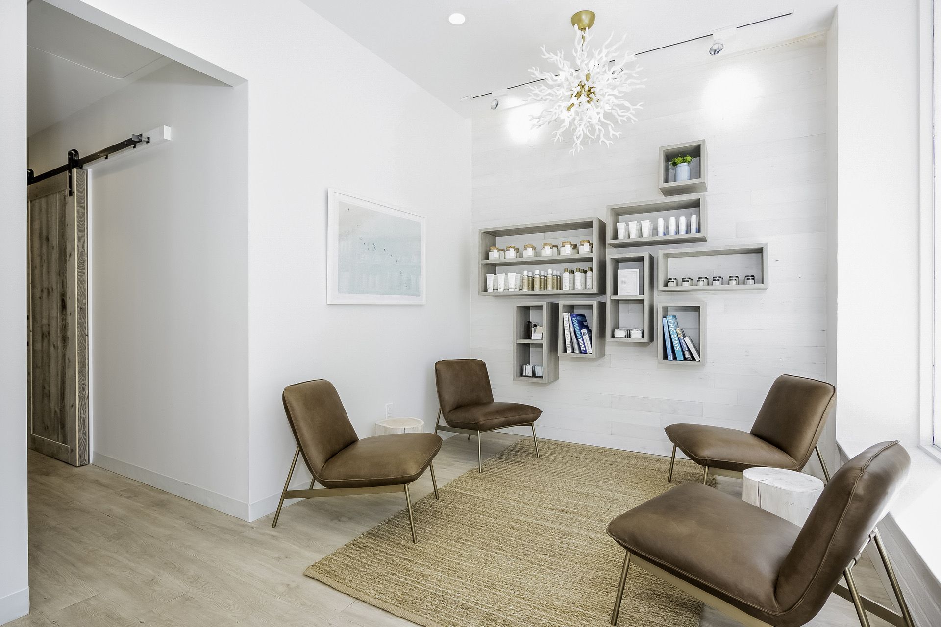 Bright white waiting room with four tan chairs, a rug, and wall shelves with decor and books.