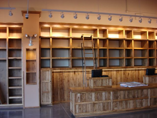 Empty wooden library or bookstore interior with built-in shelves, ladder, and a front counter under track lighting