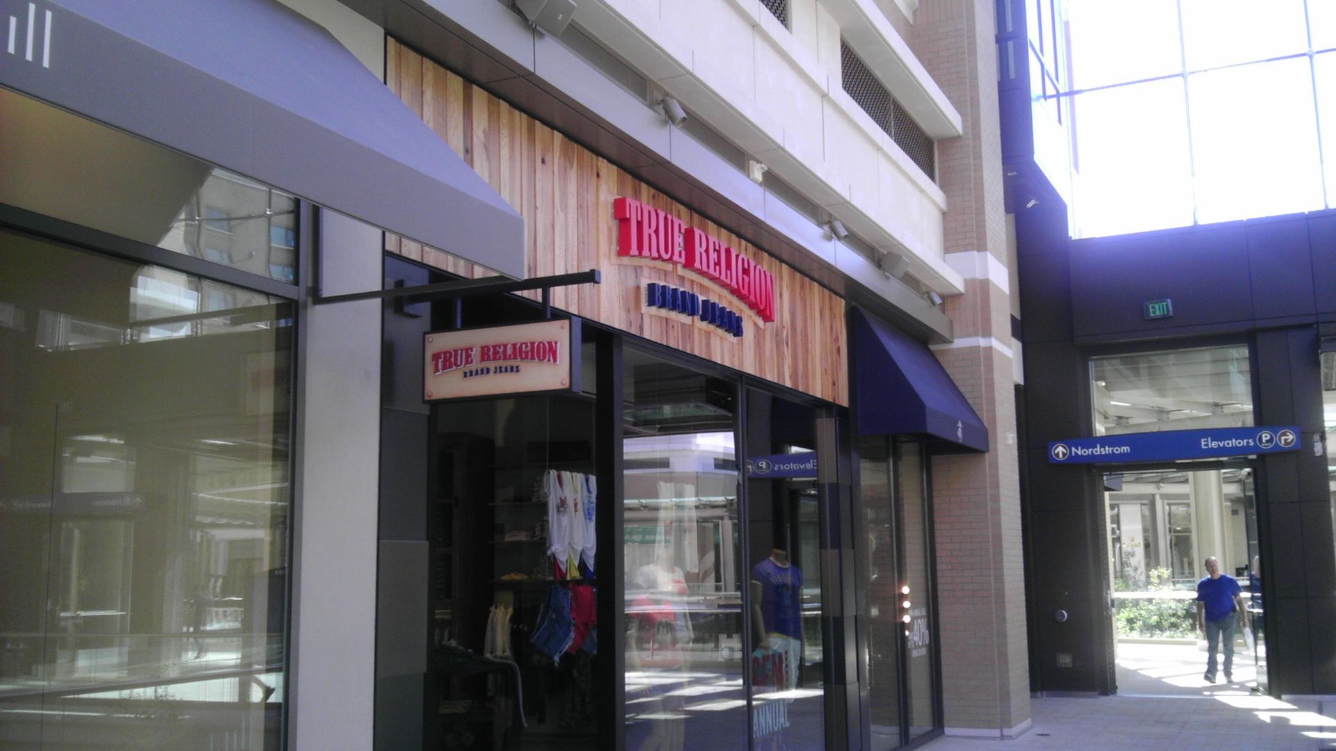Street-level storefront with glass windows and a black awning in a modern shopping walkway.