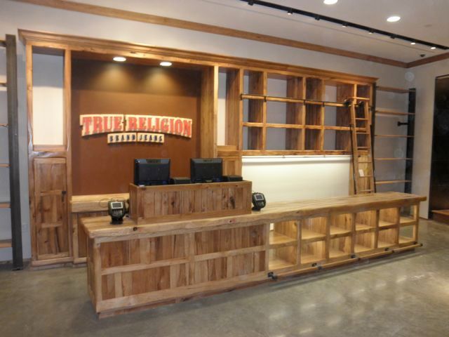 Wooden reception desk and shelving in a modern lobby with a branded sign behind the counter