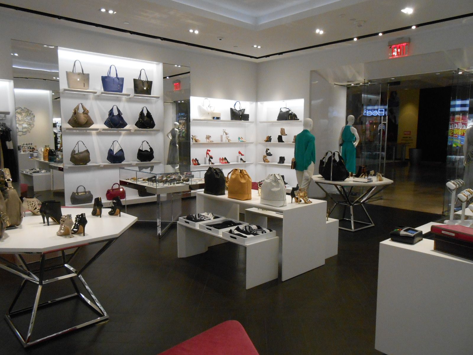 Bright retail boutique with shelves of handbags, display tables, and clothing on mannequins under recessed lighting