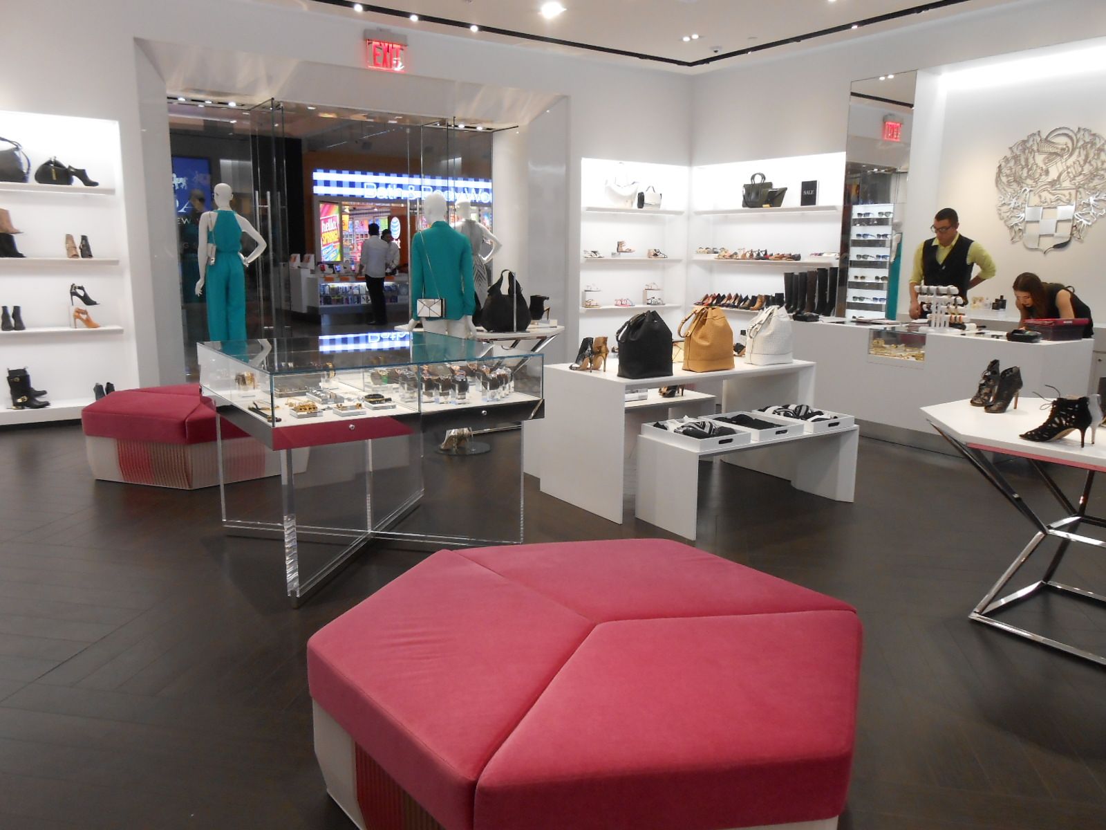 Modern boutique interior with pink ottomans, white display tables, clothing racks, and a cashier counter