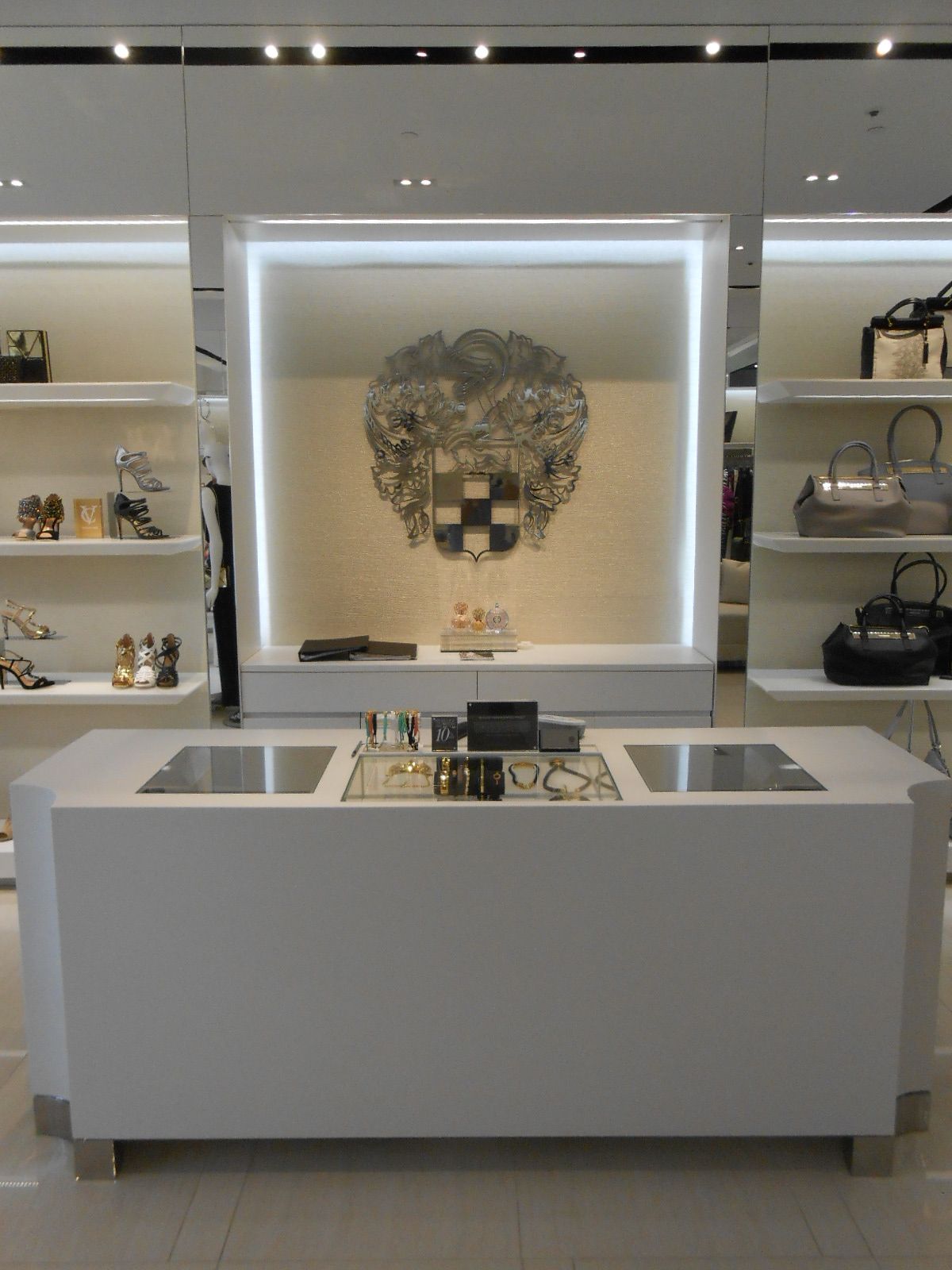 Luxury boutique display with white shelves, handbags, and a central white counter under soft lighting