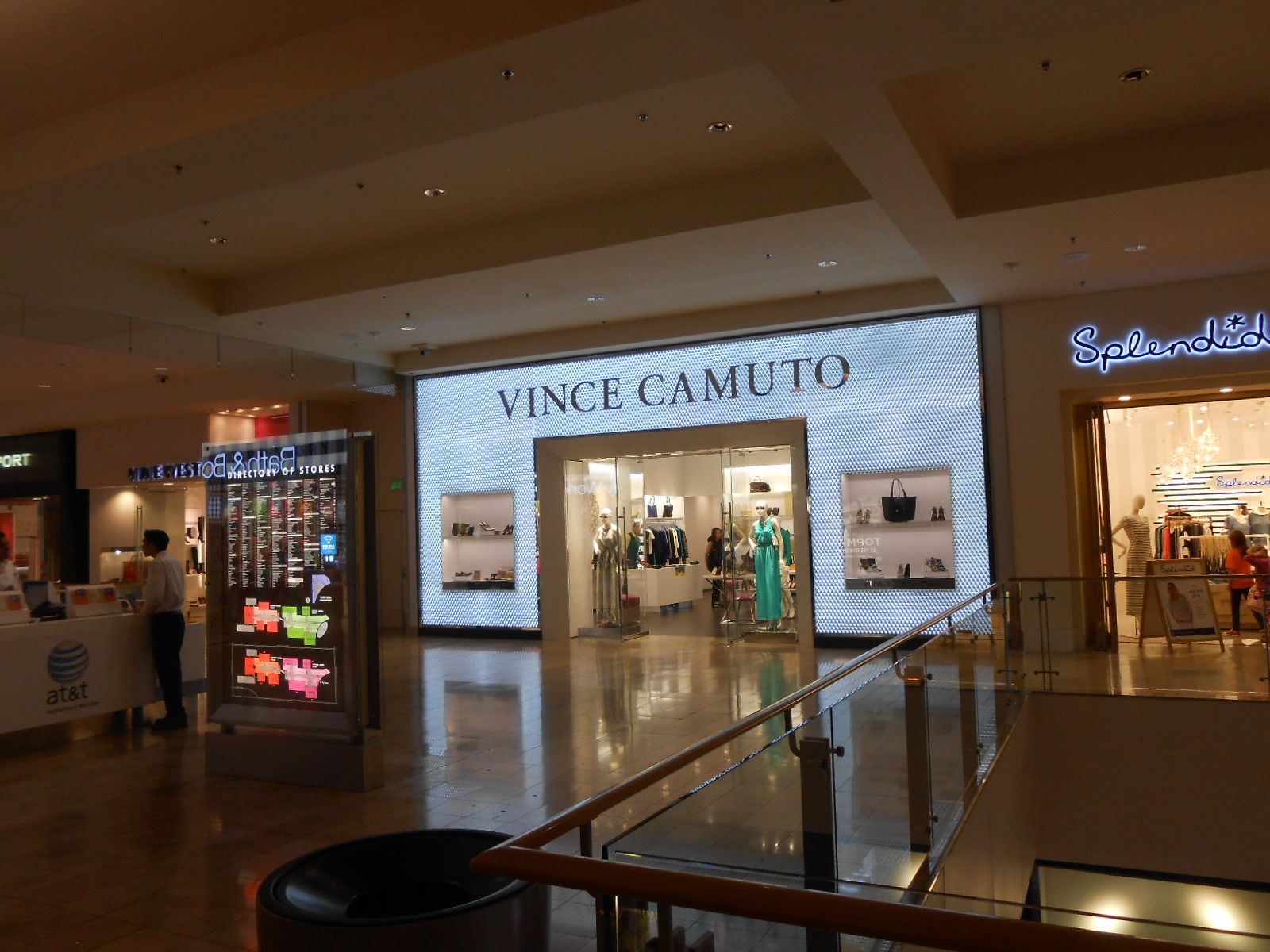Shopping mall corridor with Vince Camuto storefront and adjacent boutique, lit by warm overhead lights.