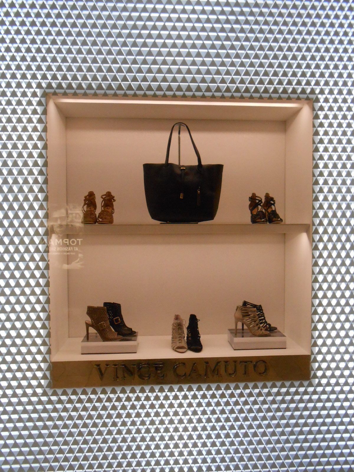 Display window with black handbag on center shelf and small shoes on upper and lower shelves