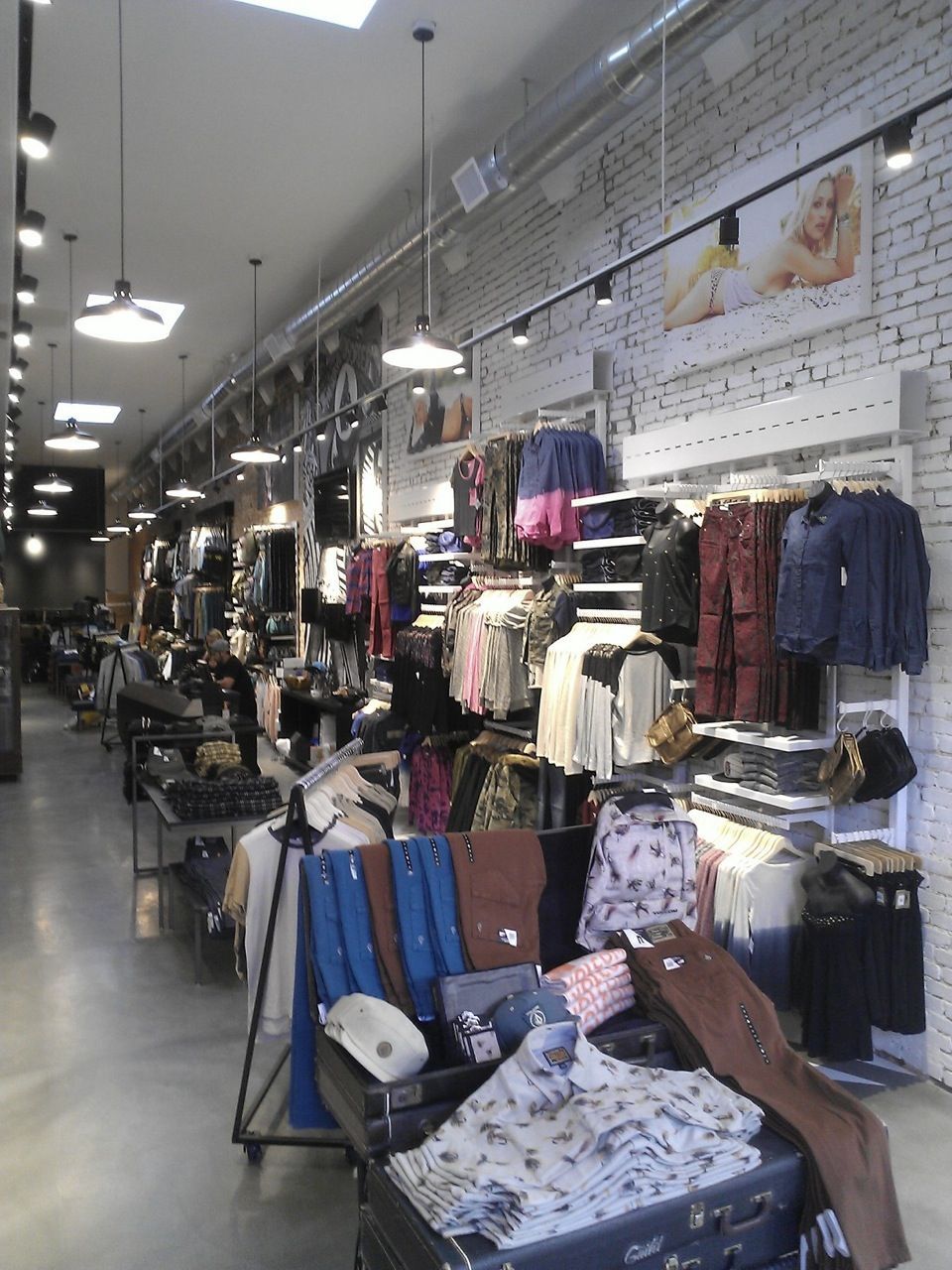 Clothing store aisle with racks of shirts, jackets, and jeans under bright ceiling lights