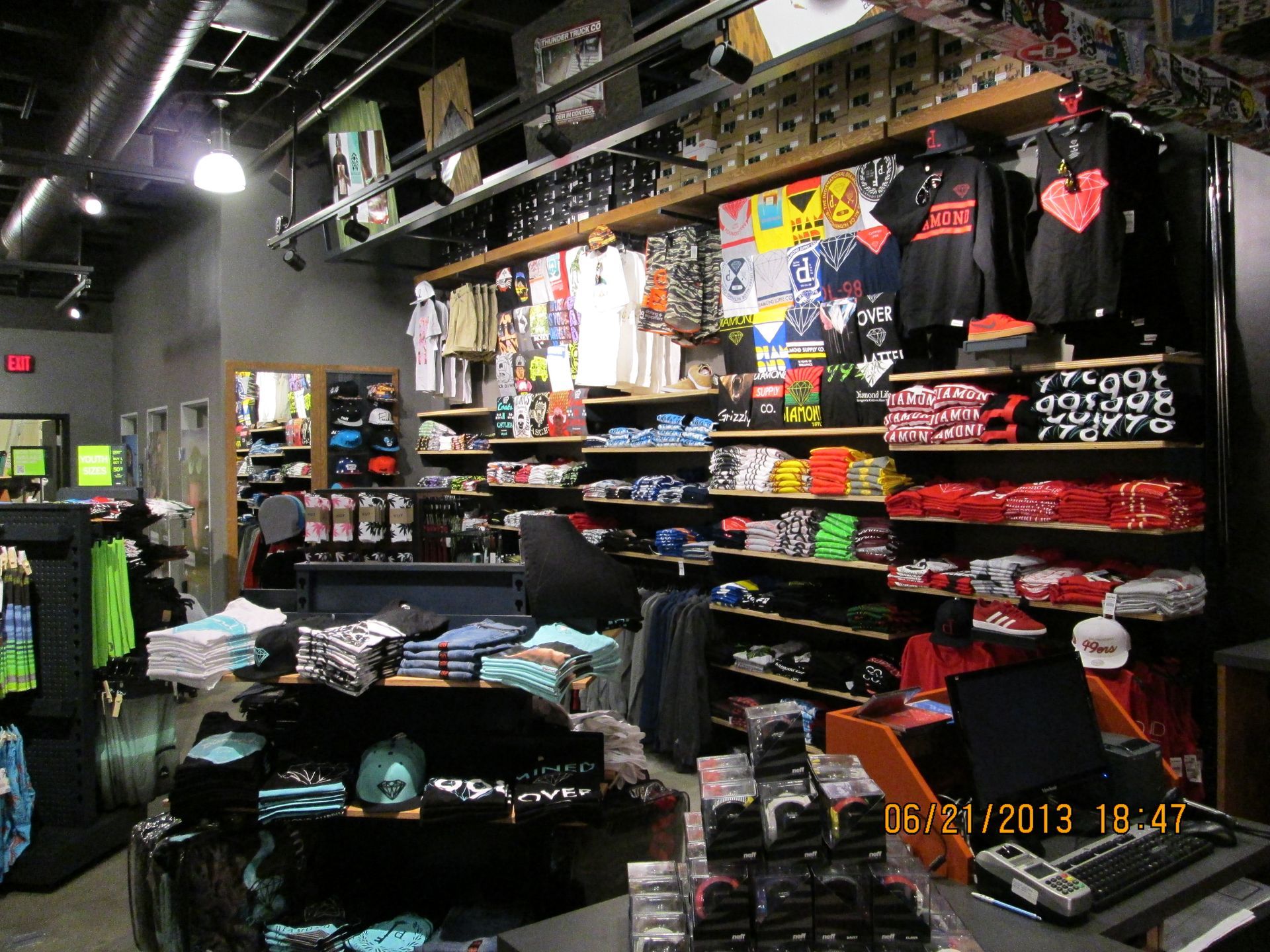 Clothing and souvenir shop interior with shelves of folded shirts, hanging apparel, and bright merchandise displays