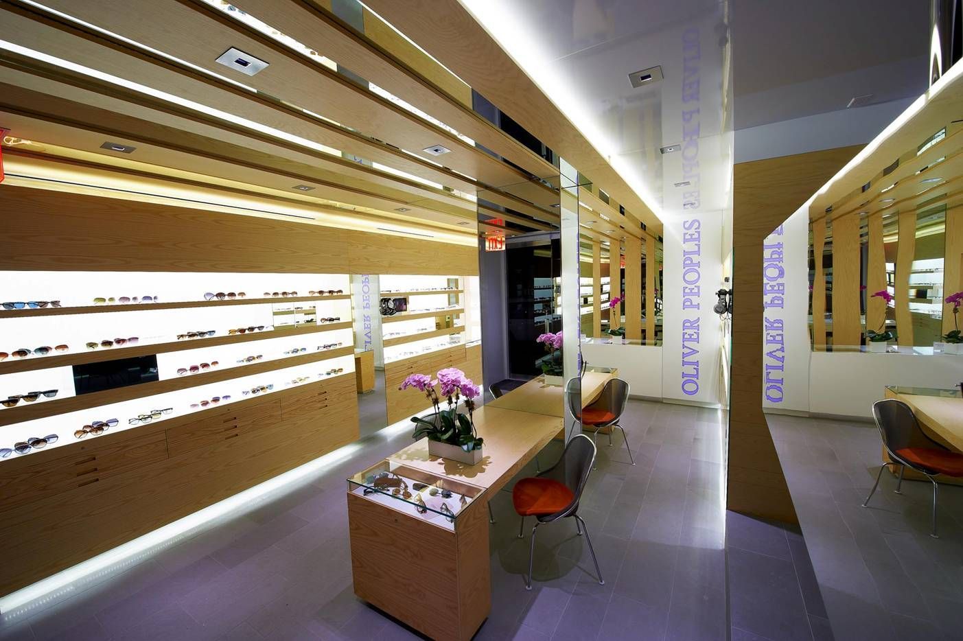 Modern hallway with wood slat walls, bright strip lighting, mirrors, and a small seating area with flowers
