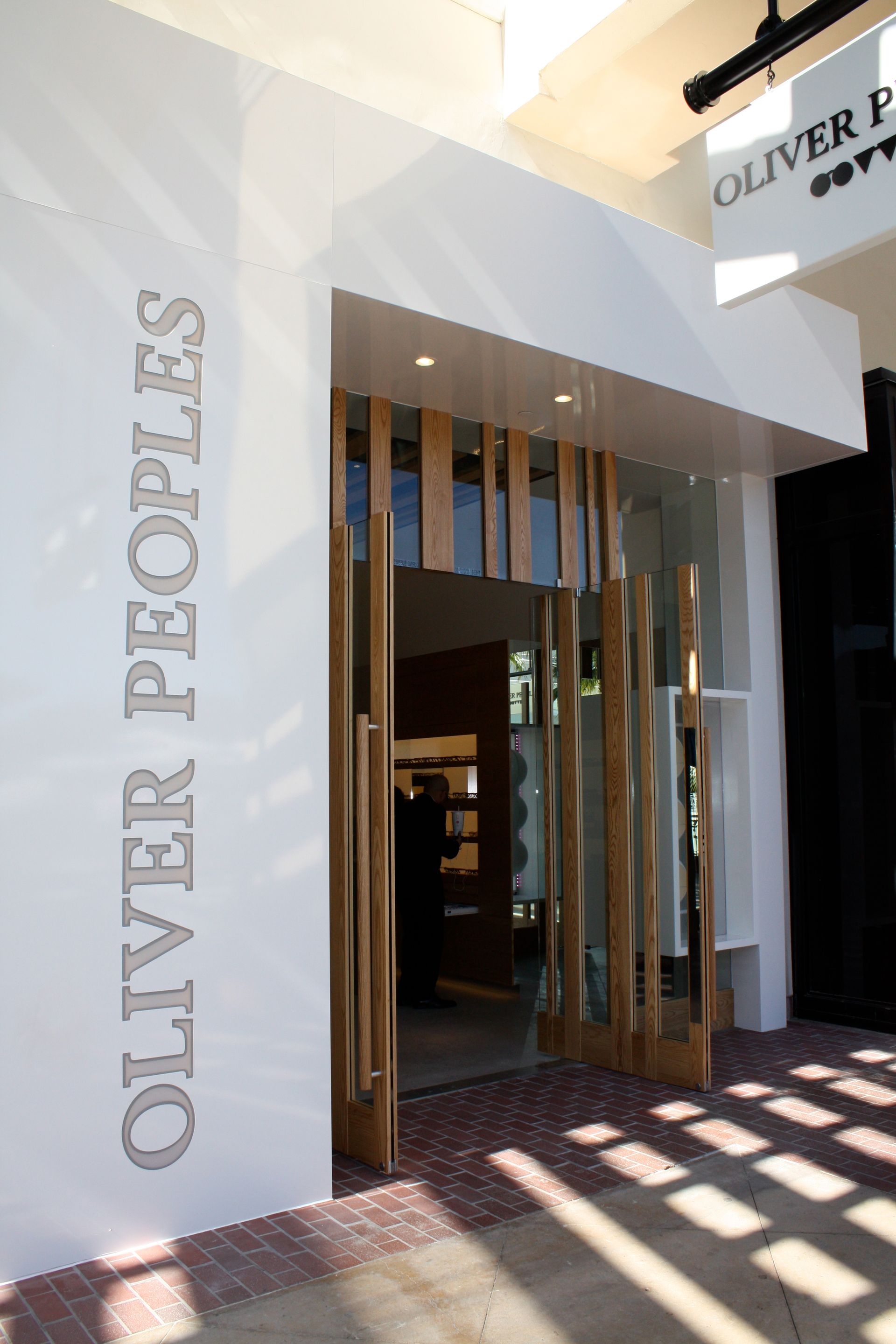 Entrance to Oliver Peoples store with white facade and wooden slatted doorway in sunlight