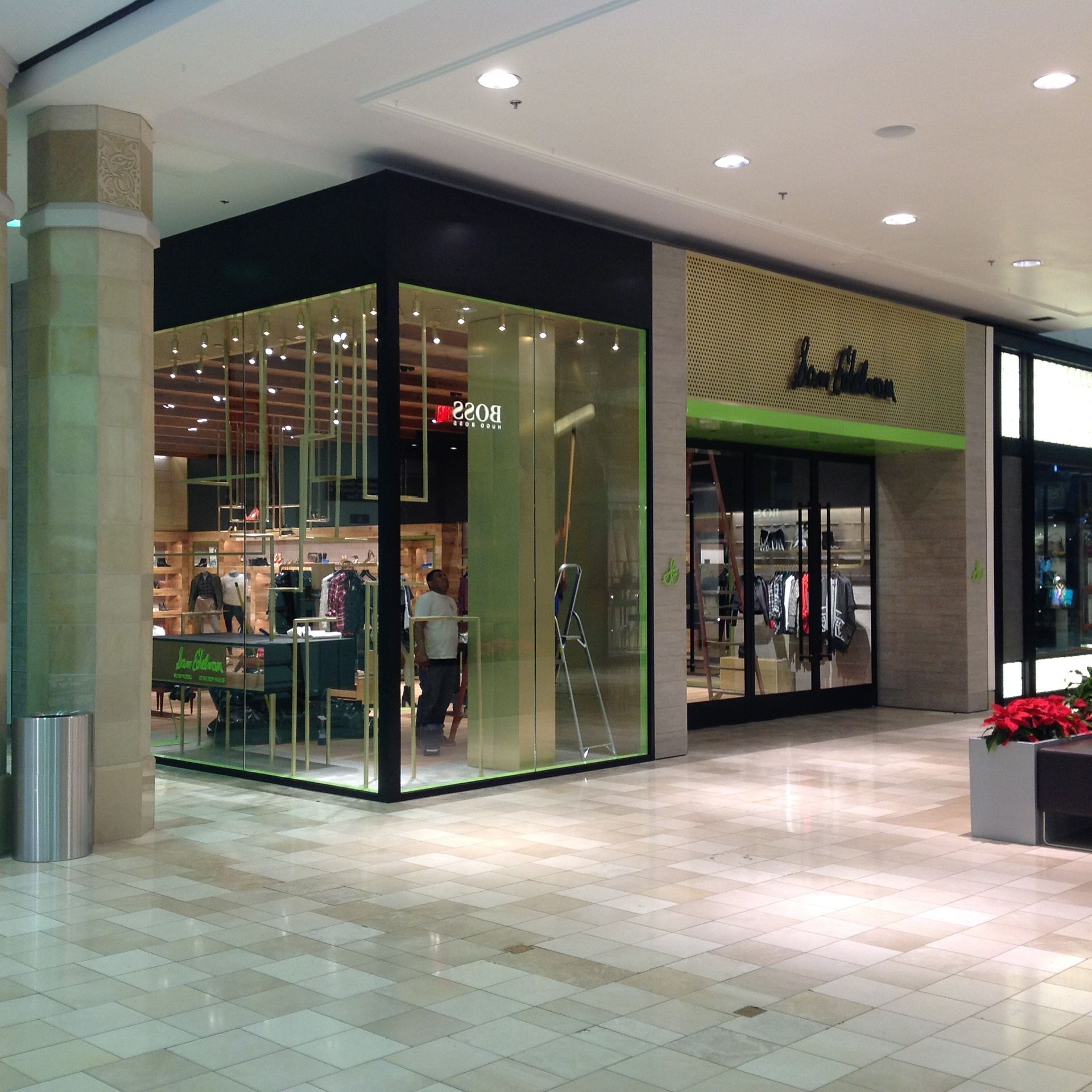 Indoor shopping mall storefront with glass walls and green trim, displaying clothing inside