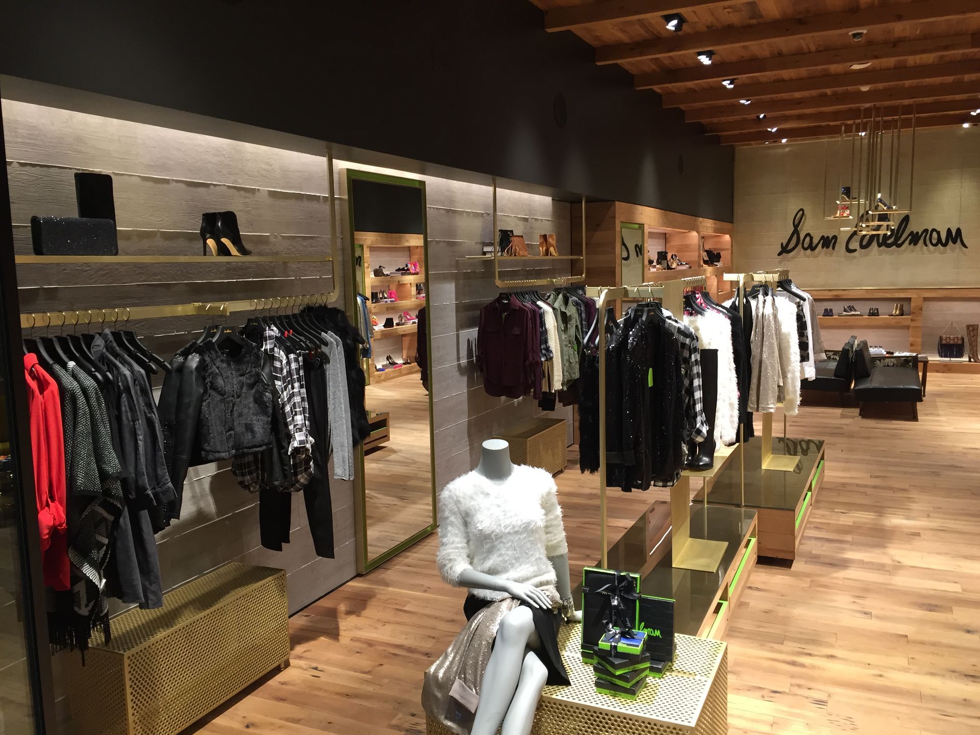 Clothing boutique interior with racks of dark and light garments, wood flooring, and a mannequin in the center.