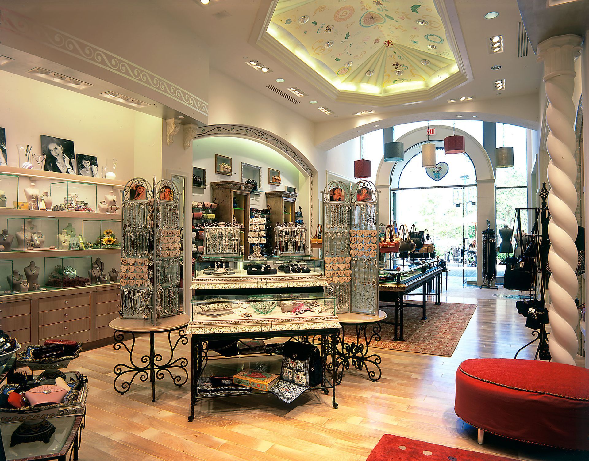 Bright boutique interior with jewelry displays, glass tables, and a red ottoman near a sunlit entrance
