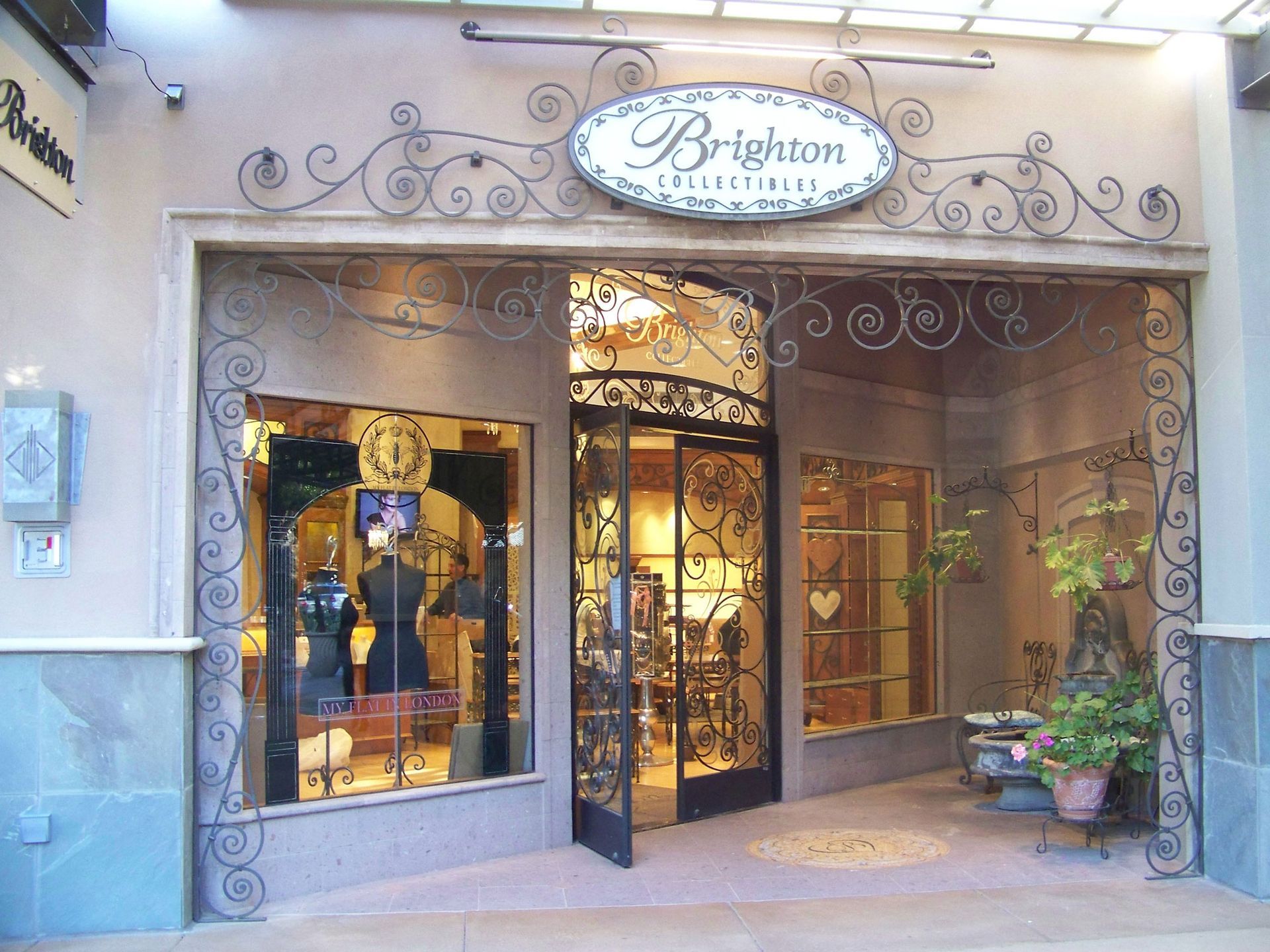 Storefront entrance with ornate ironwork, warm-lit windows, and a white oval sign above the door.
