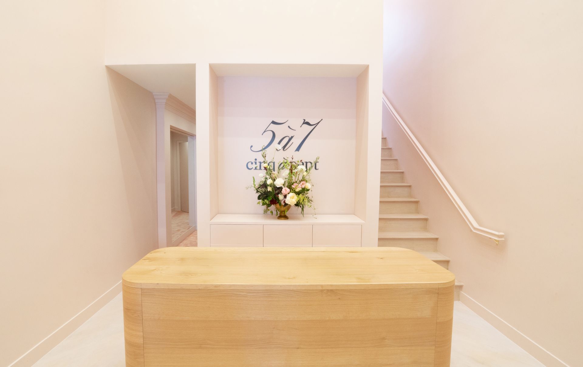 Bright hallway staircase with a wooden bench and a “57” sign with flowers on a wall shelf