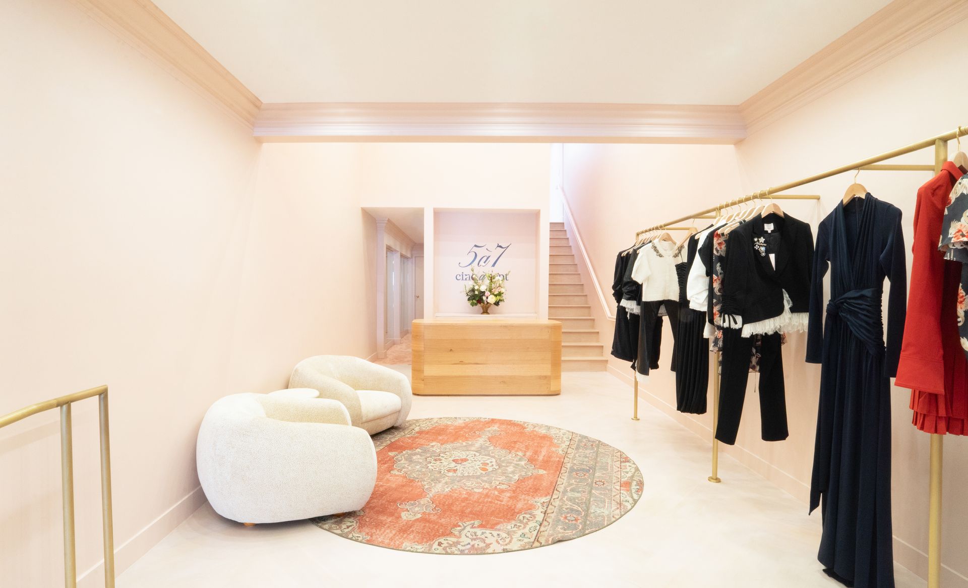 Minimalist clothing showroom with hanging garments, round rug, and cream seating in a bright room