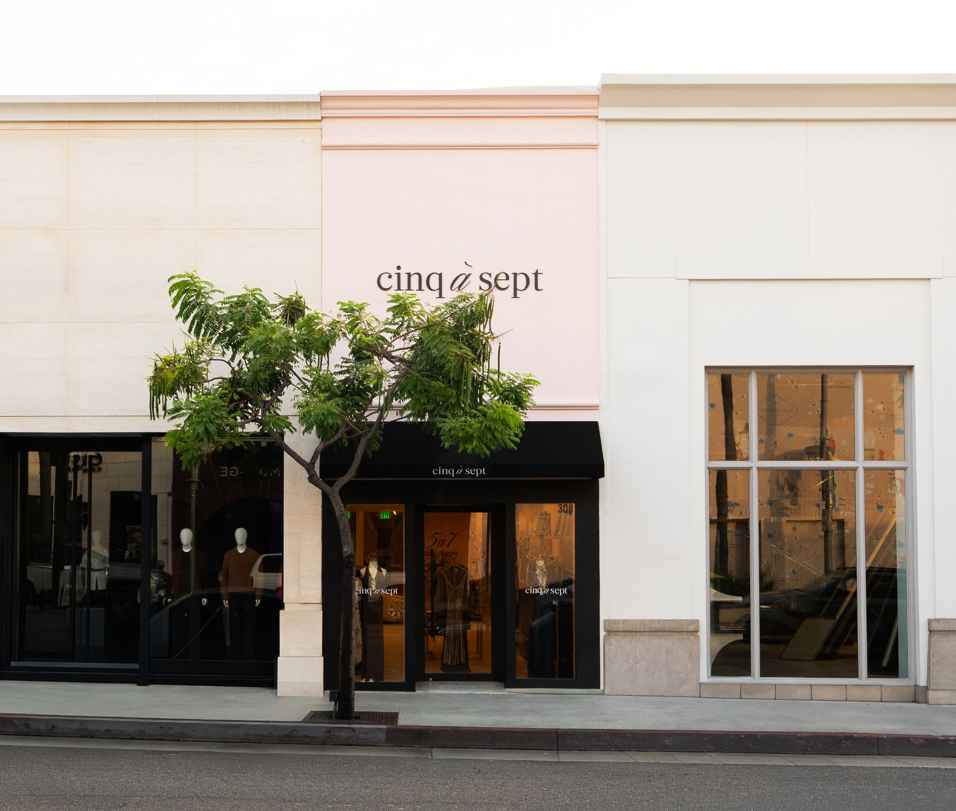 Storefront of “cinq à sept” with black awnings, white facade, and a tree in front.