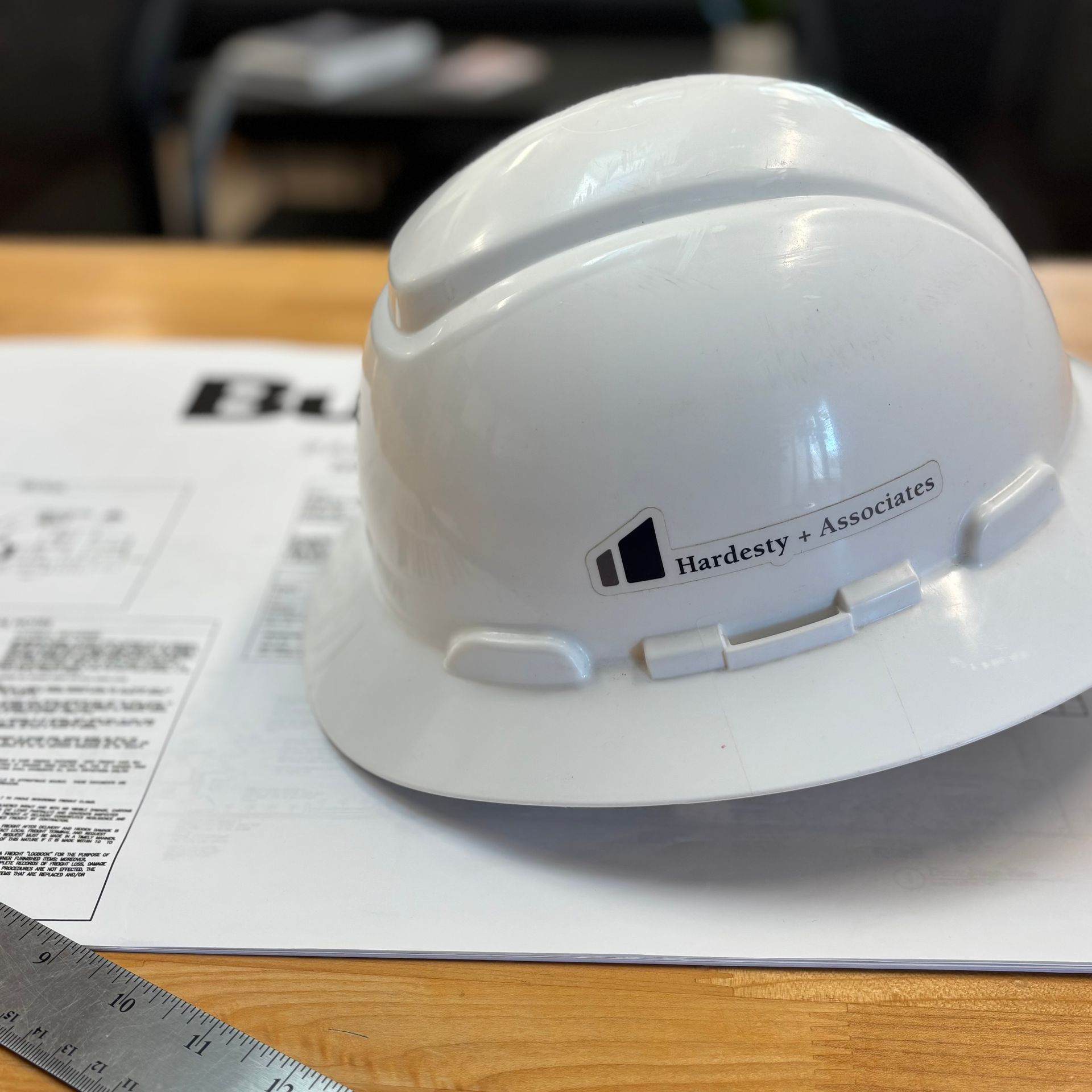 White hard hat on a desk with papers and a ruler nearby, labeled McC… & Associates