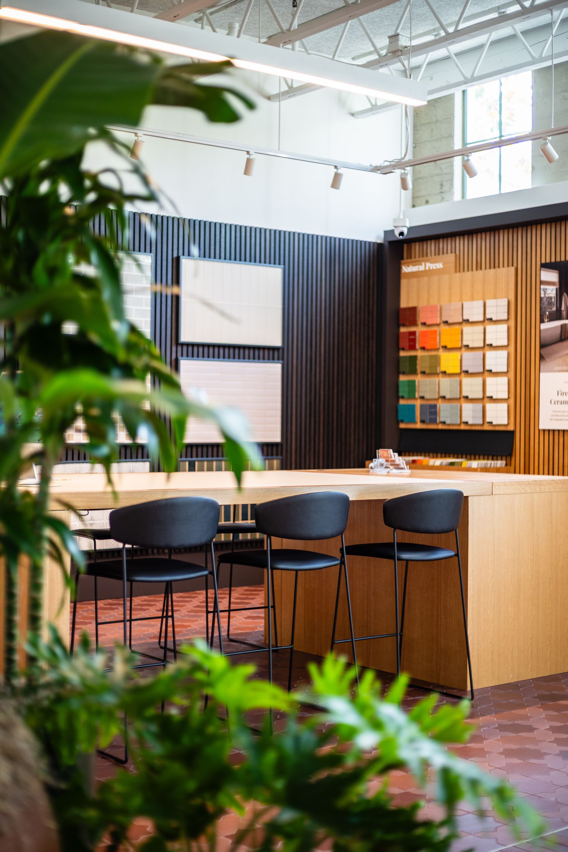 Modern office kitchen with wood bar, black stools, pendant lights, and green plants