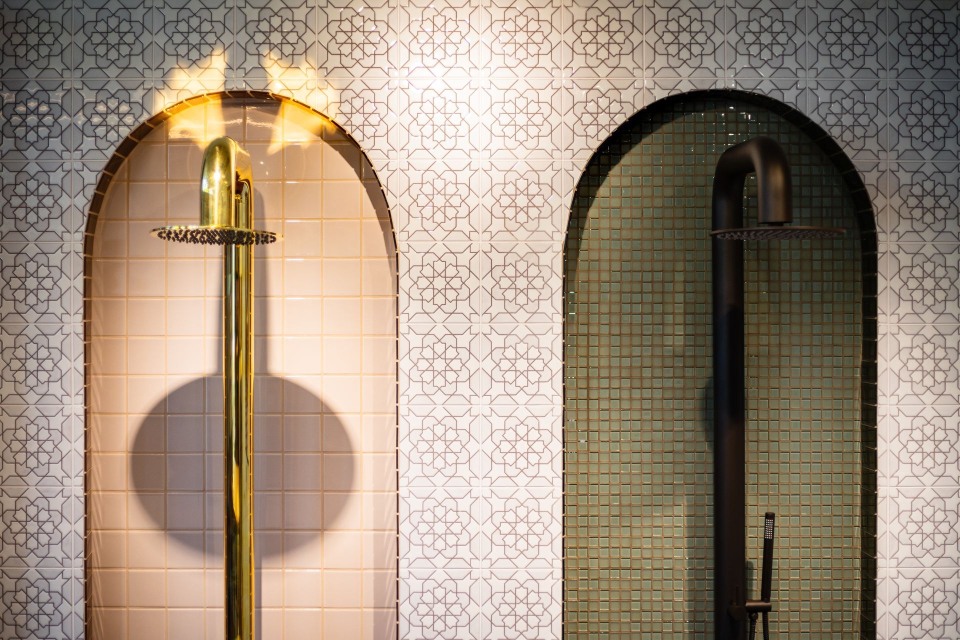 Two arched shower displays, one gold on a light patterned wall and one dark on a green tiled wall.